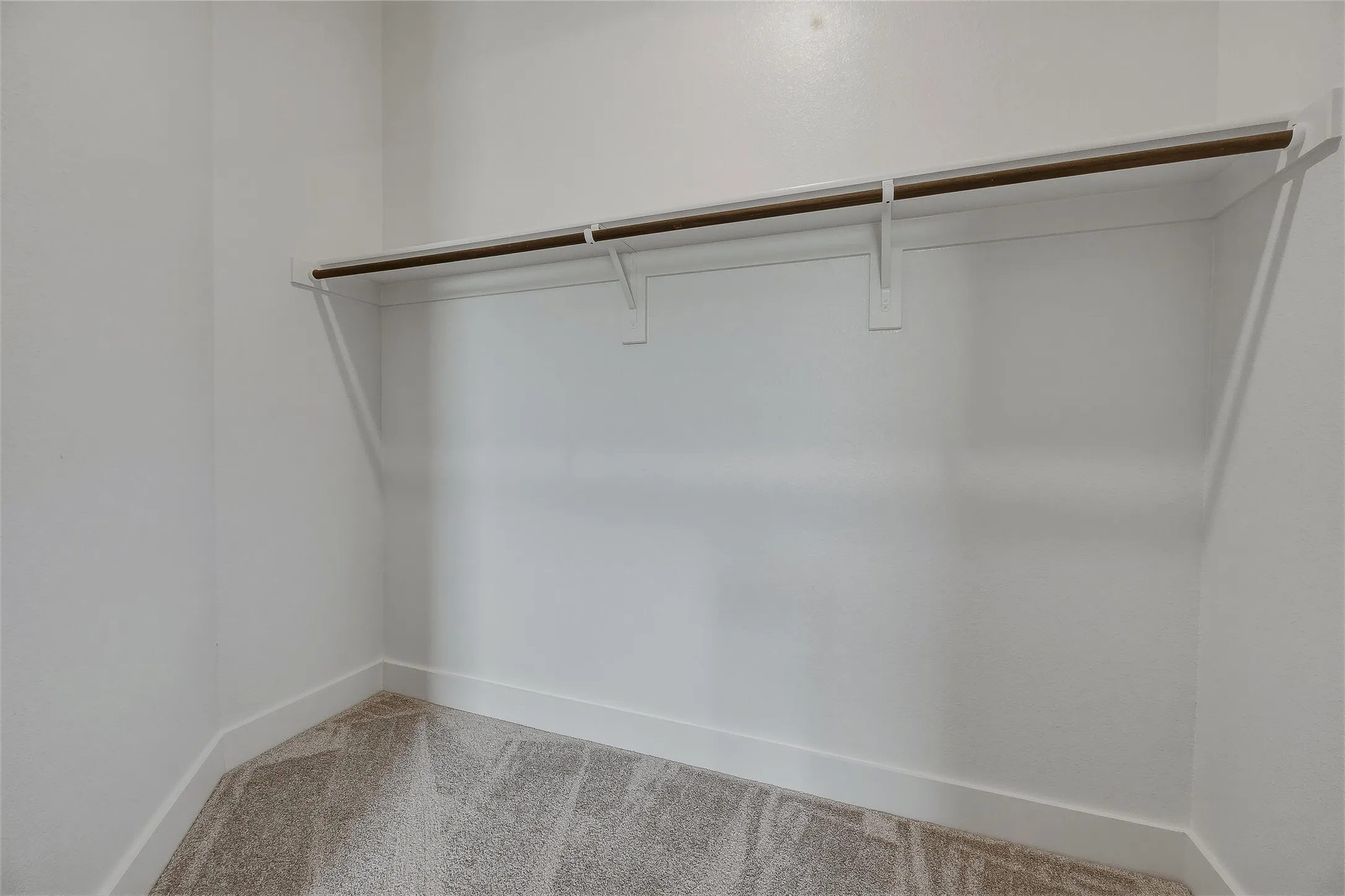 Built-in shelving with hanging rod, light neutral wall color, and carpet flooring