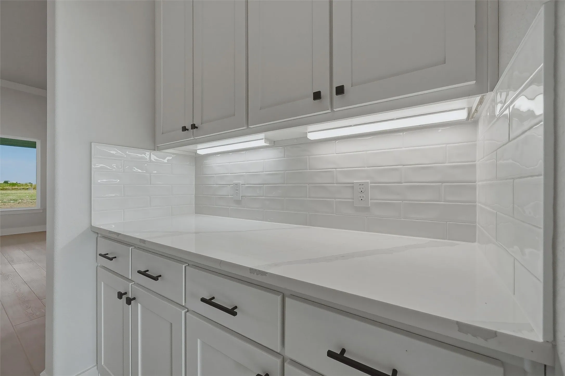 White shaker cabinetry with dark hardware, white subway tile backsplash, white countertop, and under-cabinet lighting