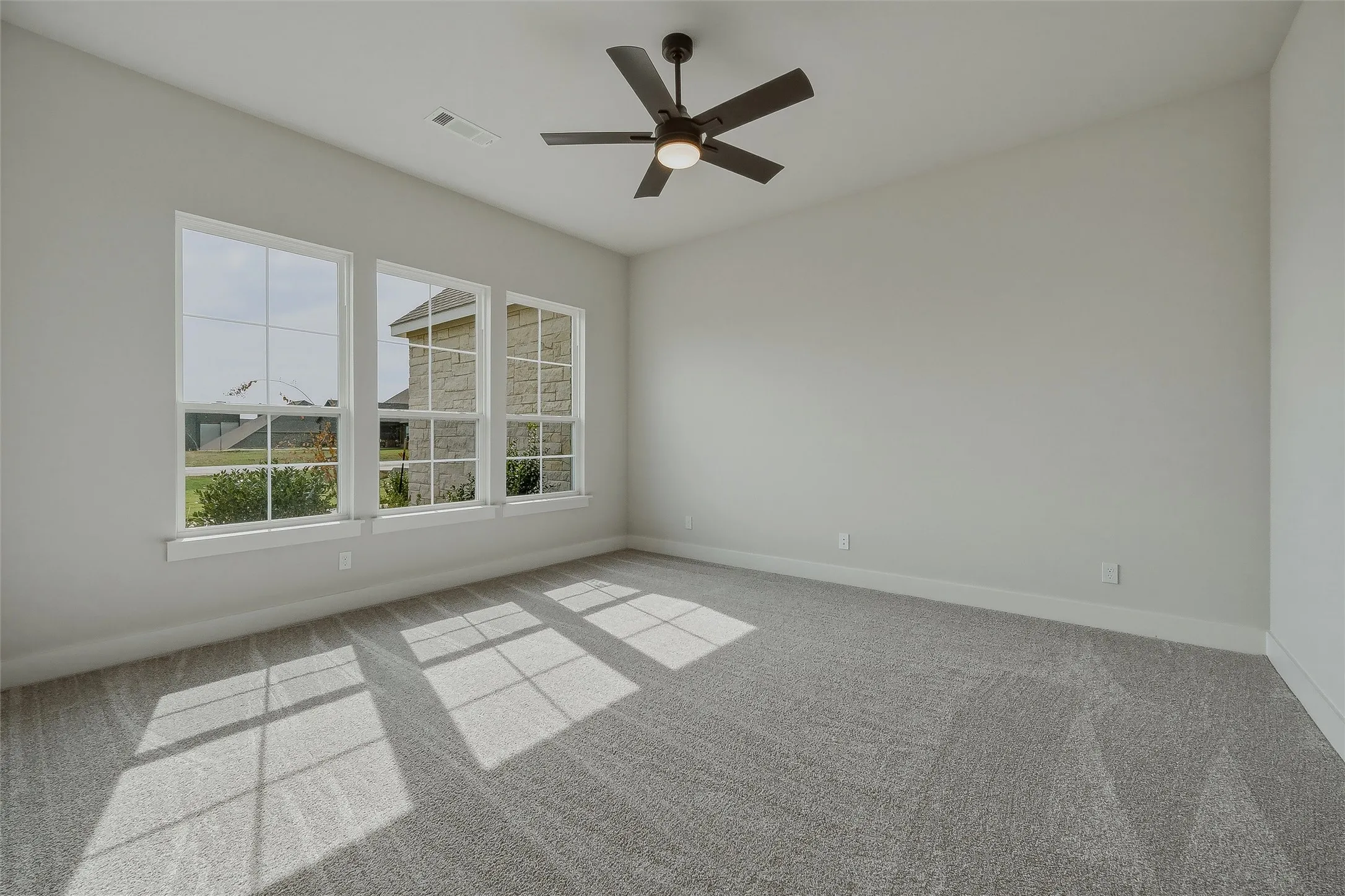 Carpeted flooring, three large windows, light gray wall paint, and a ceiling fan with integrated lighting