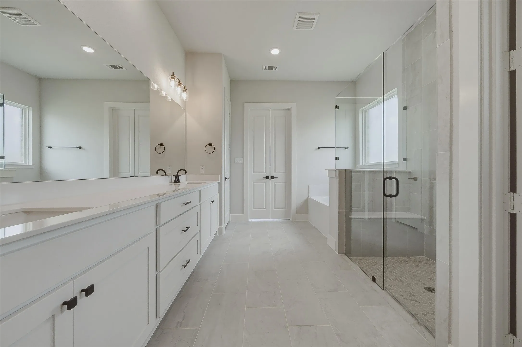 Dual vanity with white cabinetry and integrated sinks, a walk-in shower with a glass enclosure, built-in shower bench, and a separate soaking tub