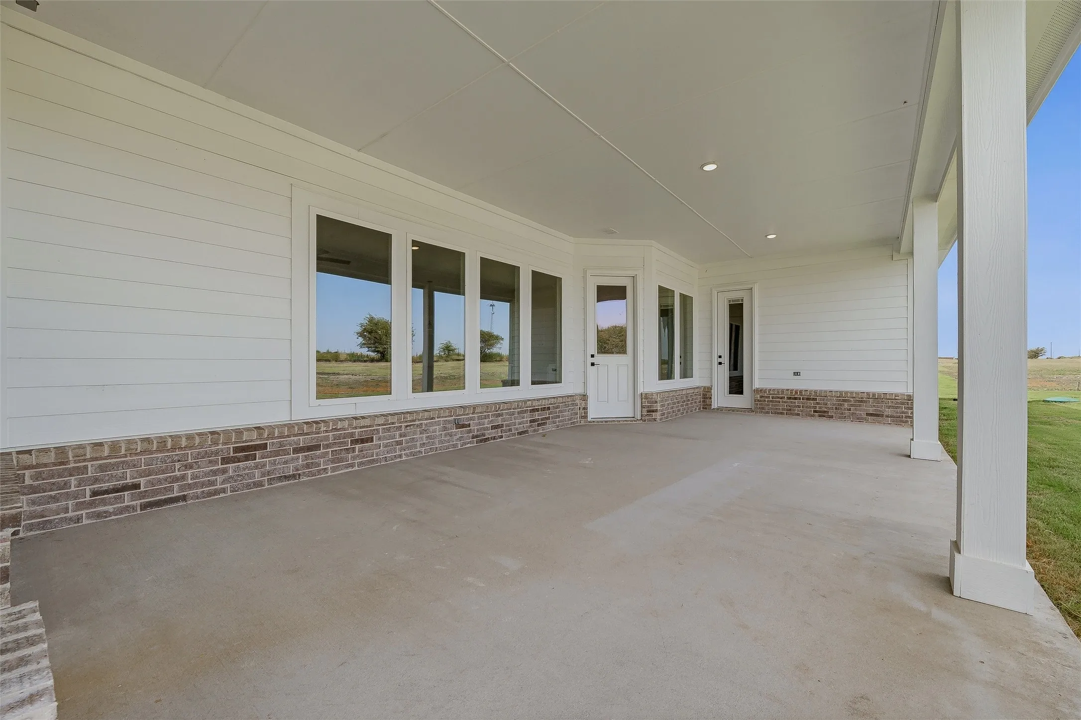 Expansive covered patio featuring a concrete surface, white siding, and a brick veneer foundation