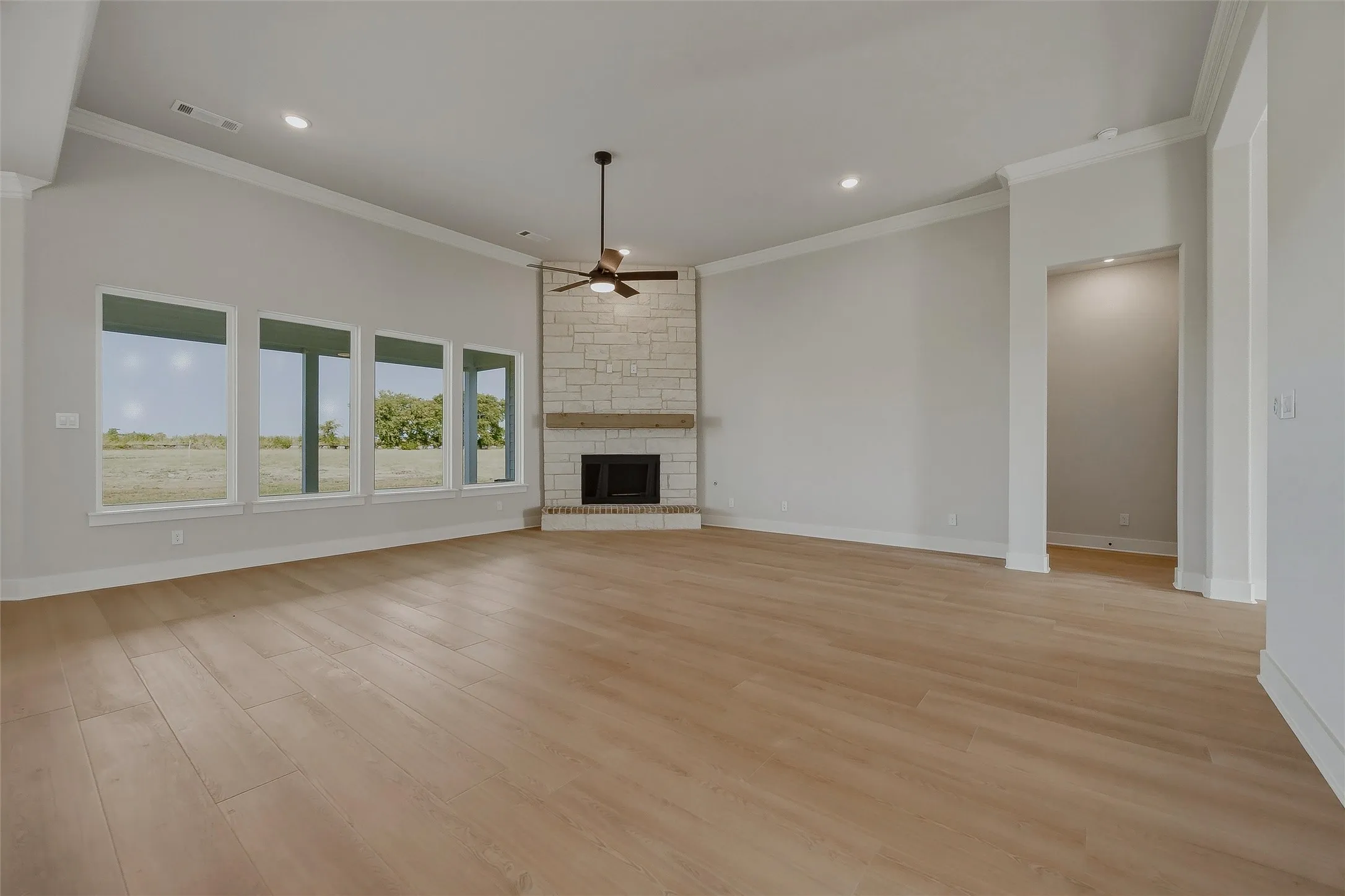 Vaulted ceiling, wood-finish flooring, stone fireplace with a wood mantle, recessed lighting, and a ceiling fan