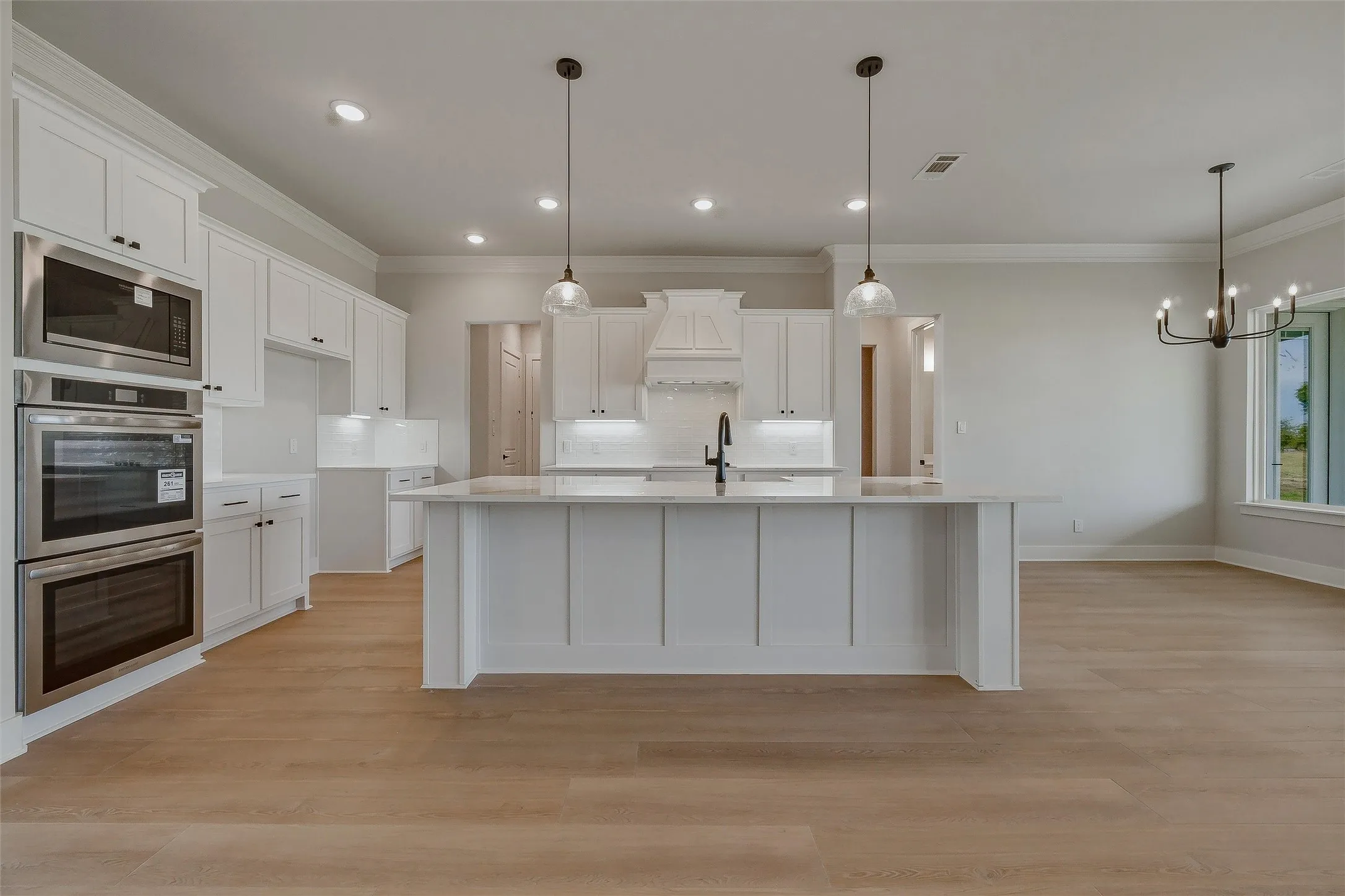 Kitchen featuring a central island, white cabinetry, integrated stainless steel appliances, pendant lighting, and wood-finish flooring