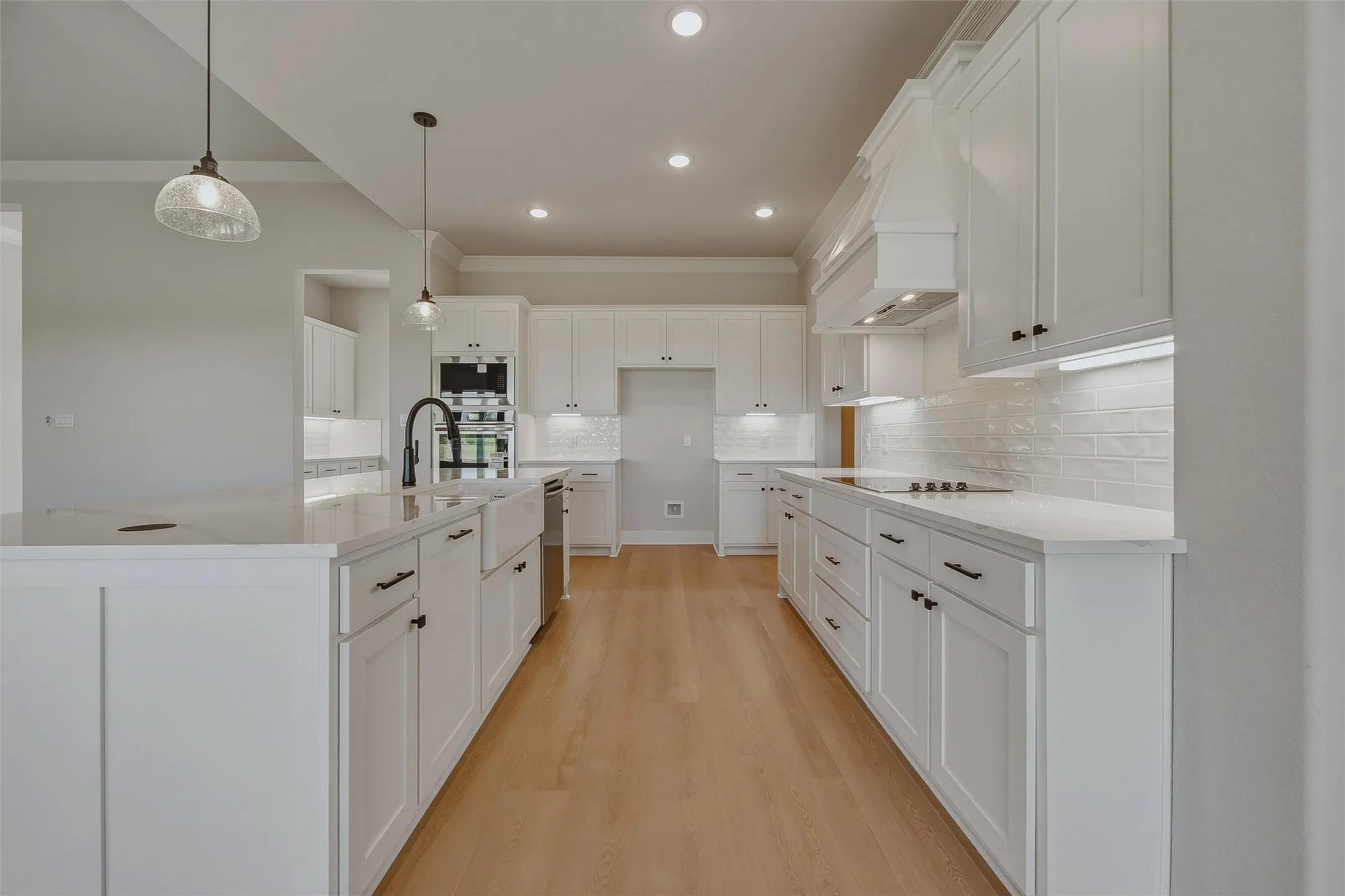 Bright kitchen featuring white shaker cabinetry, light wood-finish flooring, white subway tile backsplash, and a large central island with a farmhouse sink
