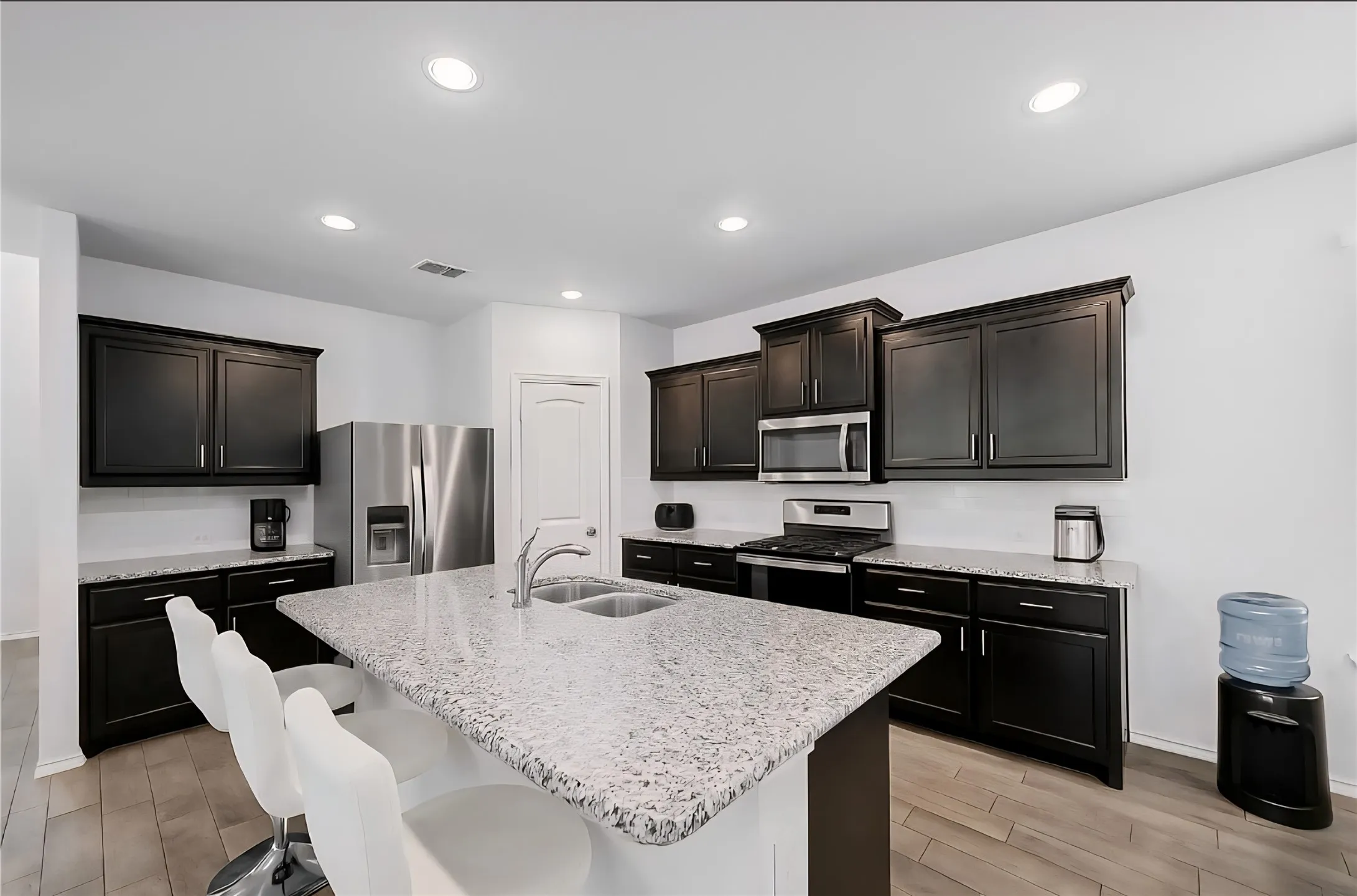 Kitchen with appliances with stainless steel finishes, a kitchen bar, light stone countertops, wood finish floors, and recessed lighting