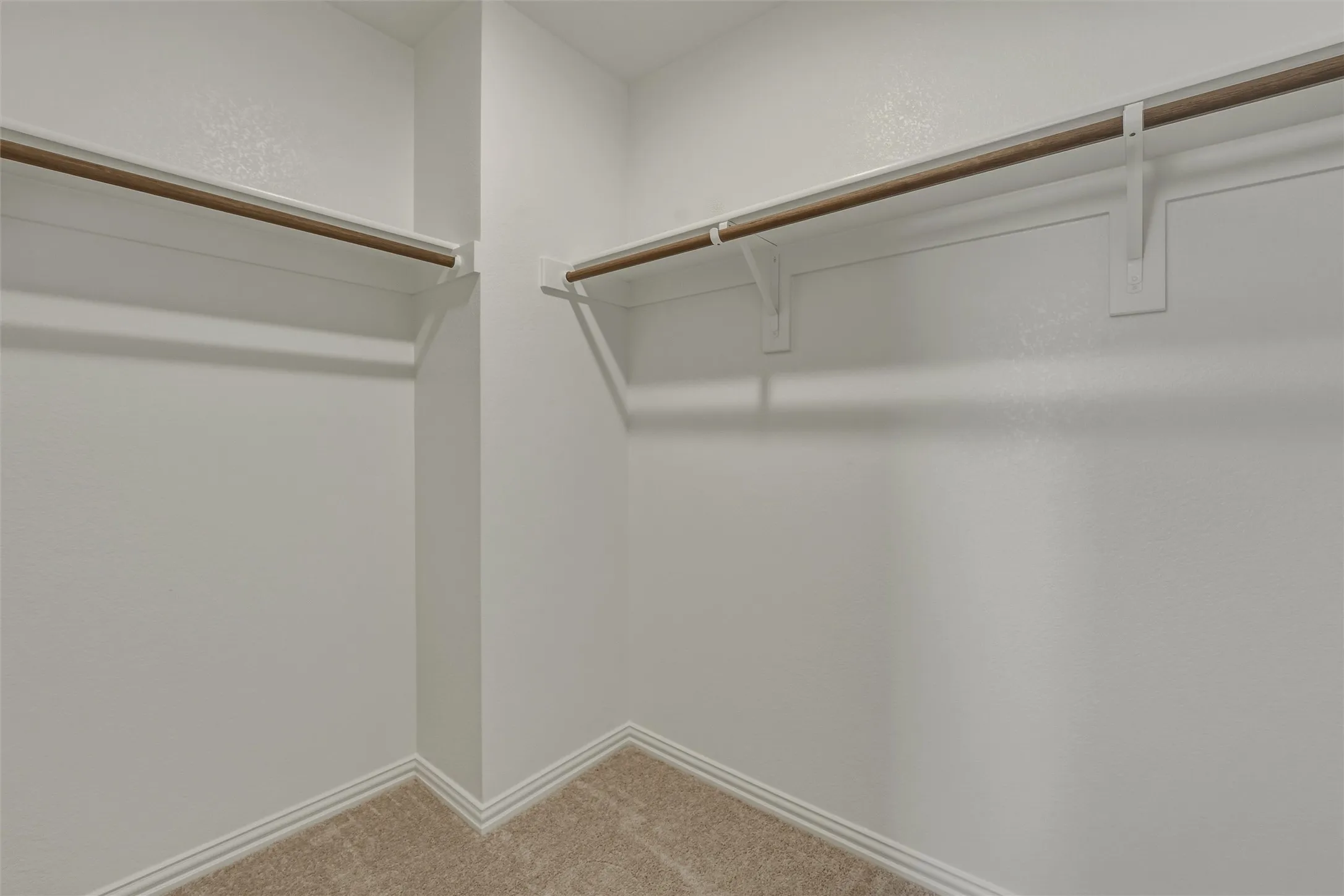 Walk-in closet featuring light beige carpeting, white walls, white baseboards, and two levels of wood-finish hanging rods