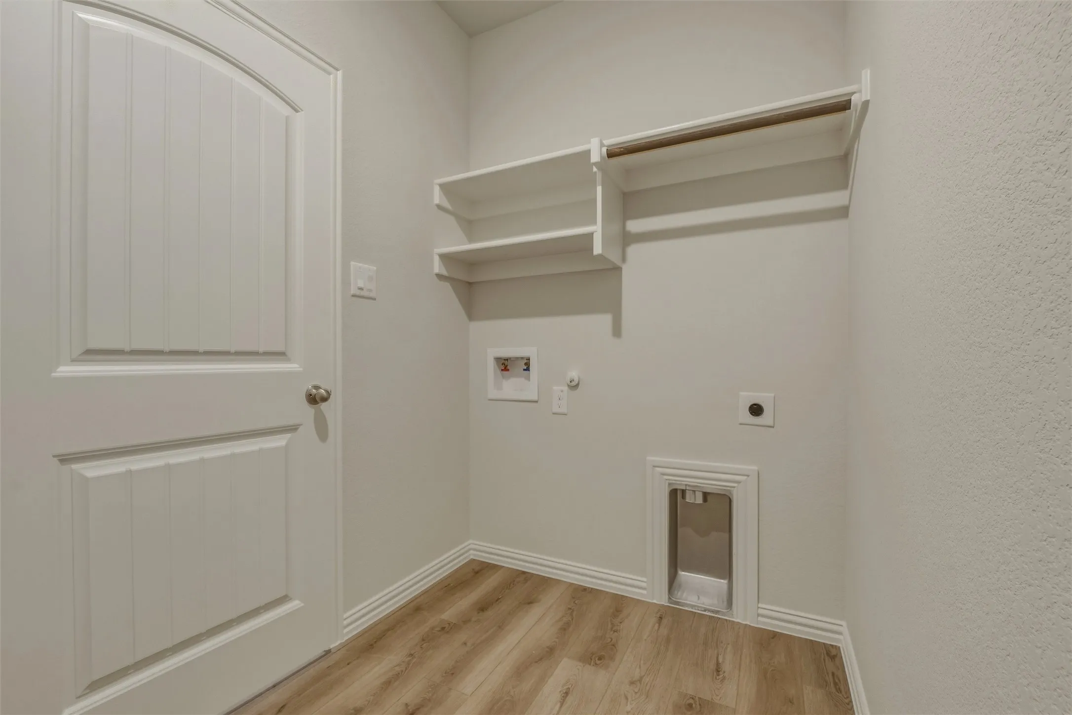 Dedicated laundry space featuring wood-finish flooring, white walls, and built-in shelving with a hanging rod