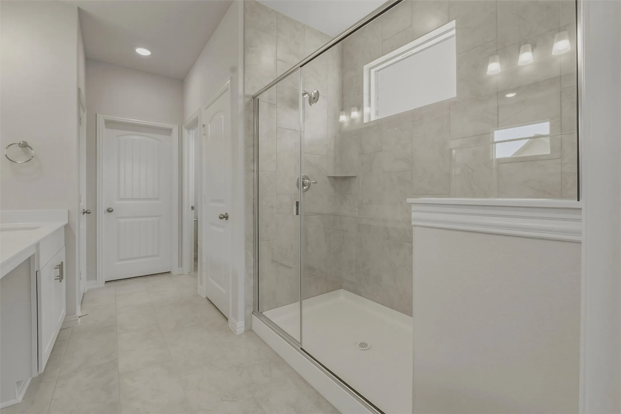 Enclosed shower with full-height tile surround and glass enclosure, featuring a built-in shower niche, transom window, and contemporary vanity lighting