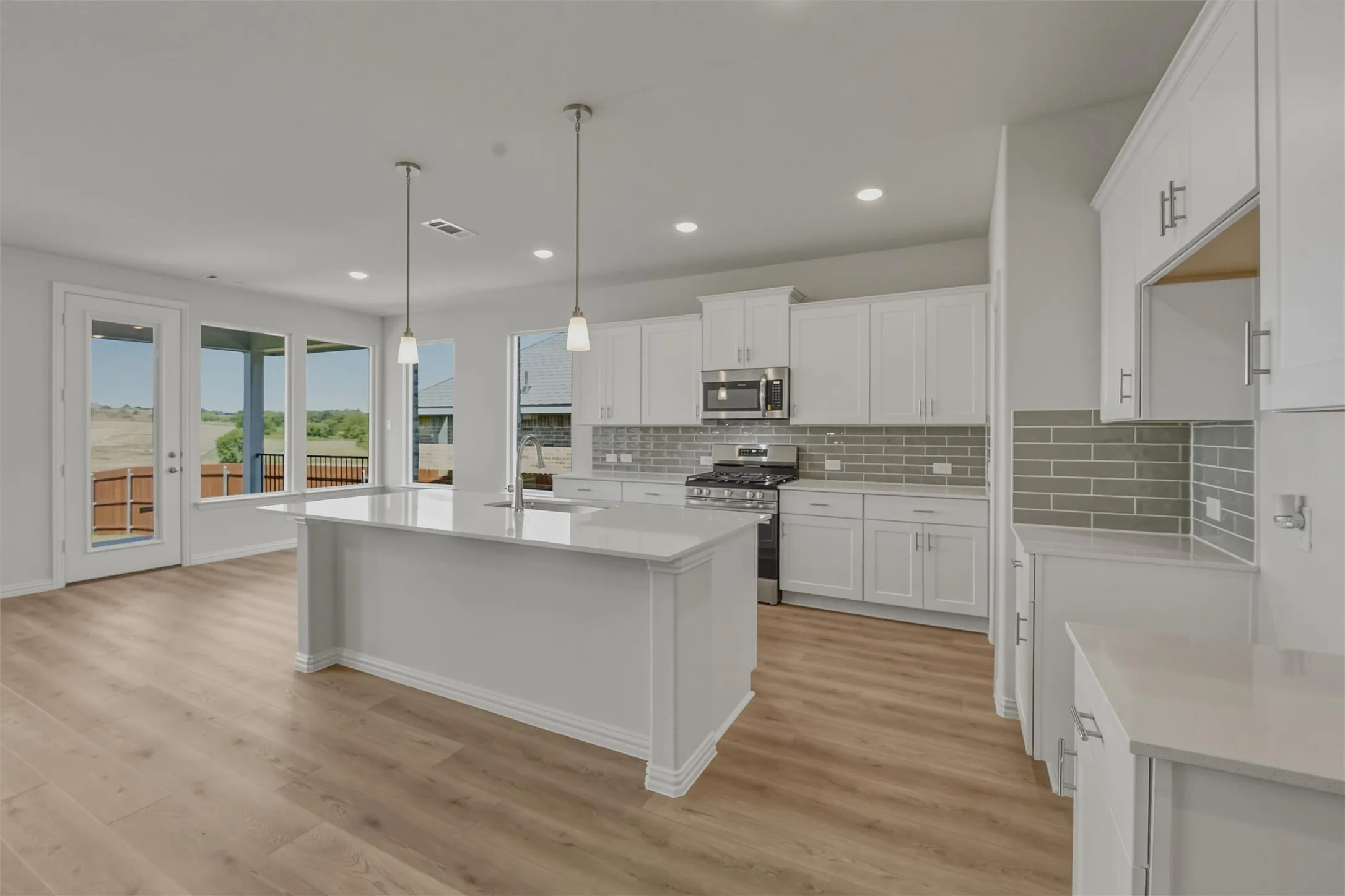 Open-concept kitchen featuring white cabinetry, light-toned countertops, and a gray subway tile backsplash