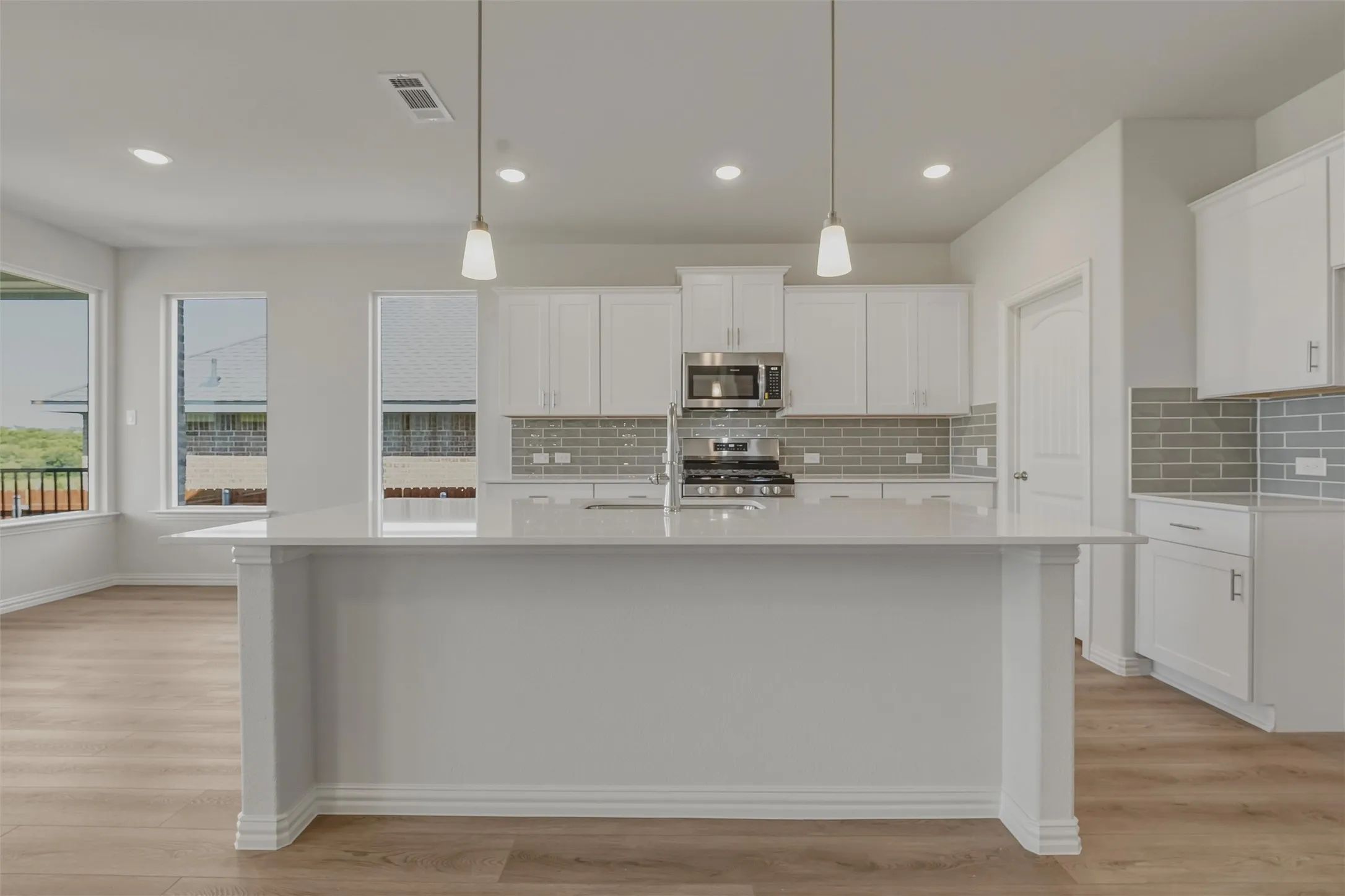 Spacious kitchen featuring an expansive island with a white countertop, white cabinetry with silver hardware, a gray subway tile backsplash, stainless steel appliances, and wood-finish flooring