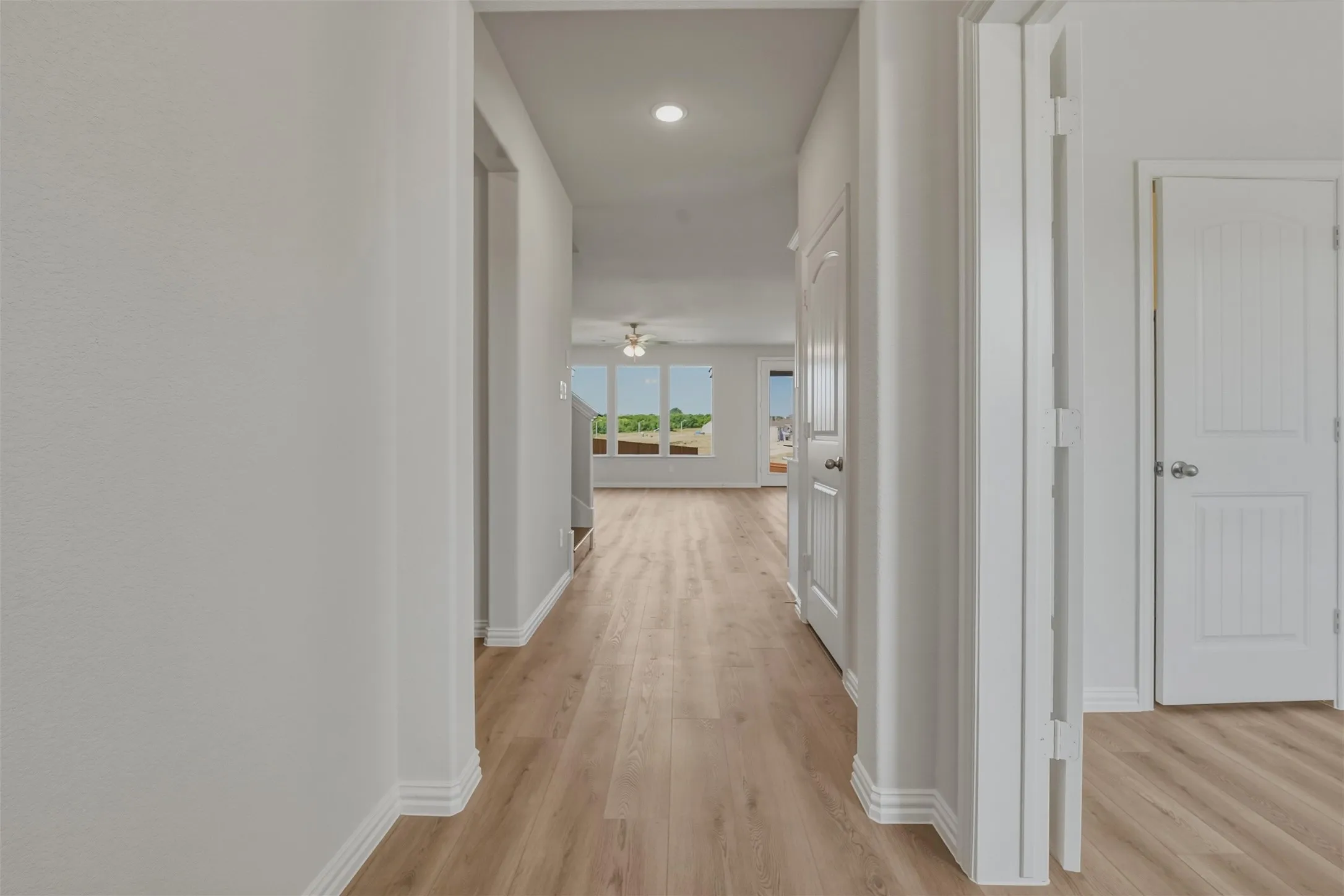 Hallway featuring wood-finish flooring, white baseboards, and white paneled doors