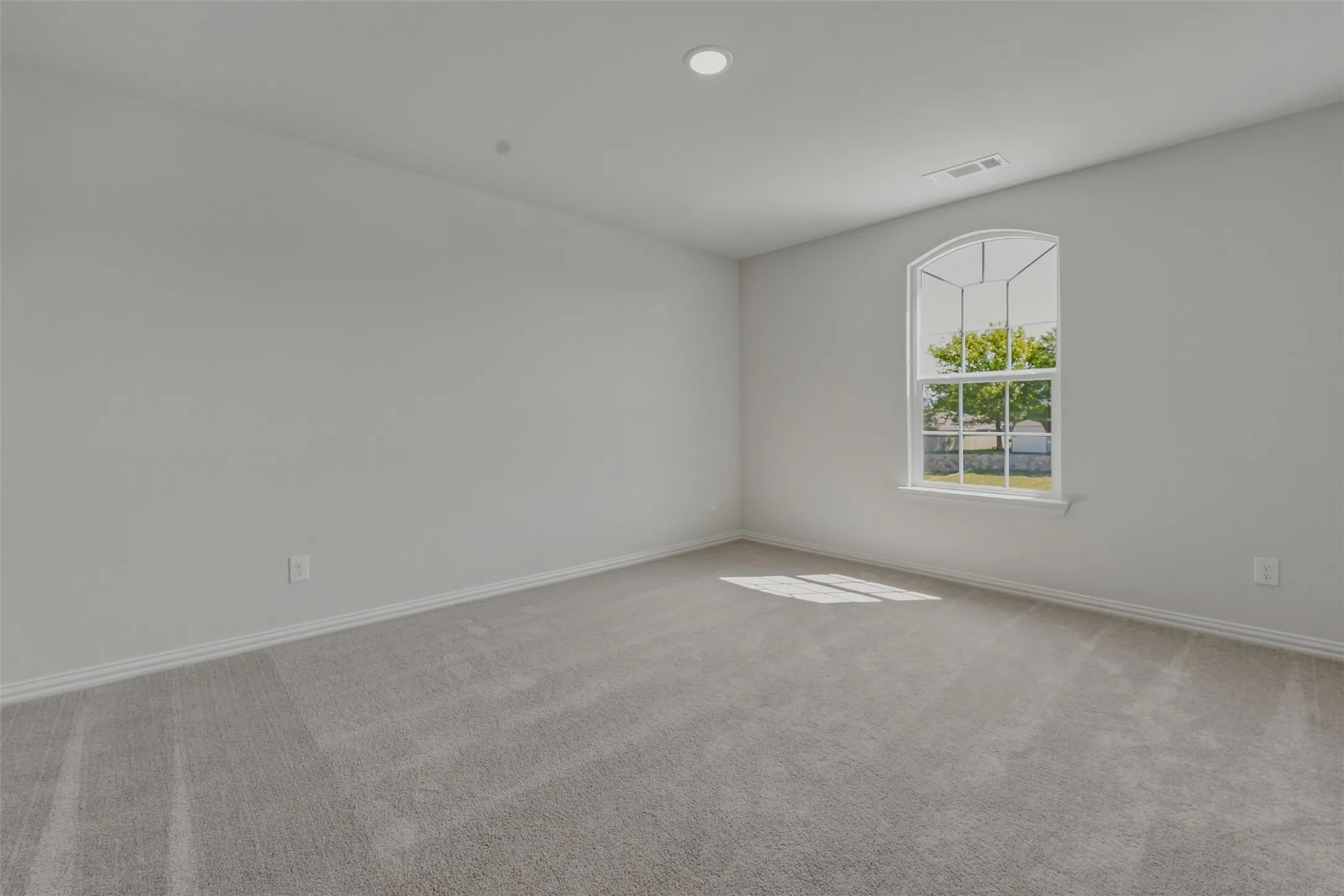 Spacious room featuring light gray carpeting, a large arched window, recessed lighting, and crisp white baseboards