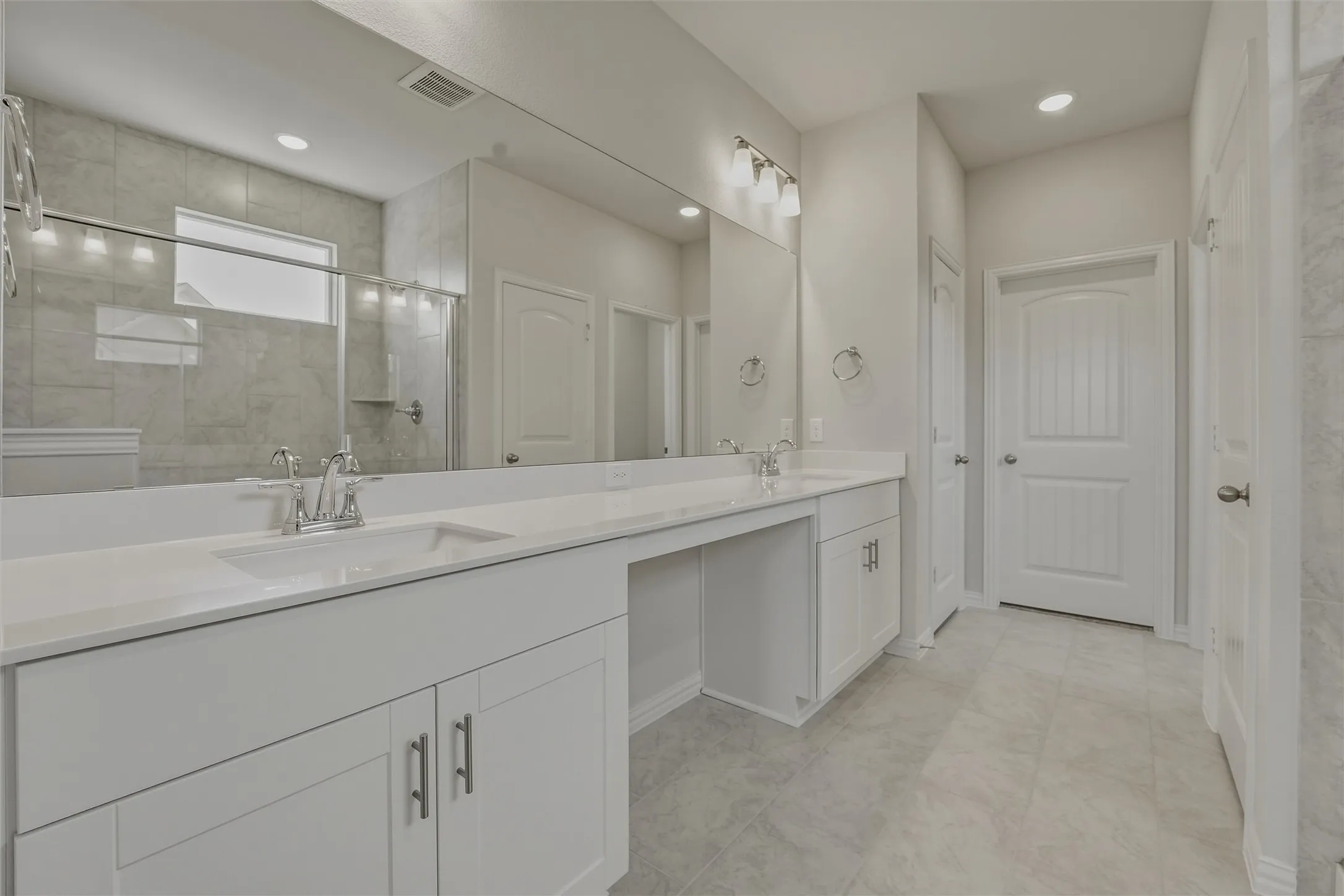 Spacious bathroom featuring a dual vanity with white cabinetry and light-toned countertops, a large frameless mirror, and a tiled walk-in shower with a glass enclosure