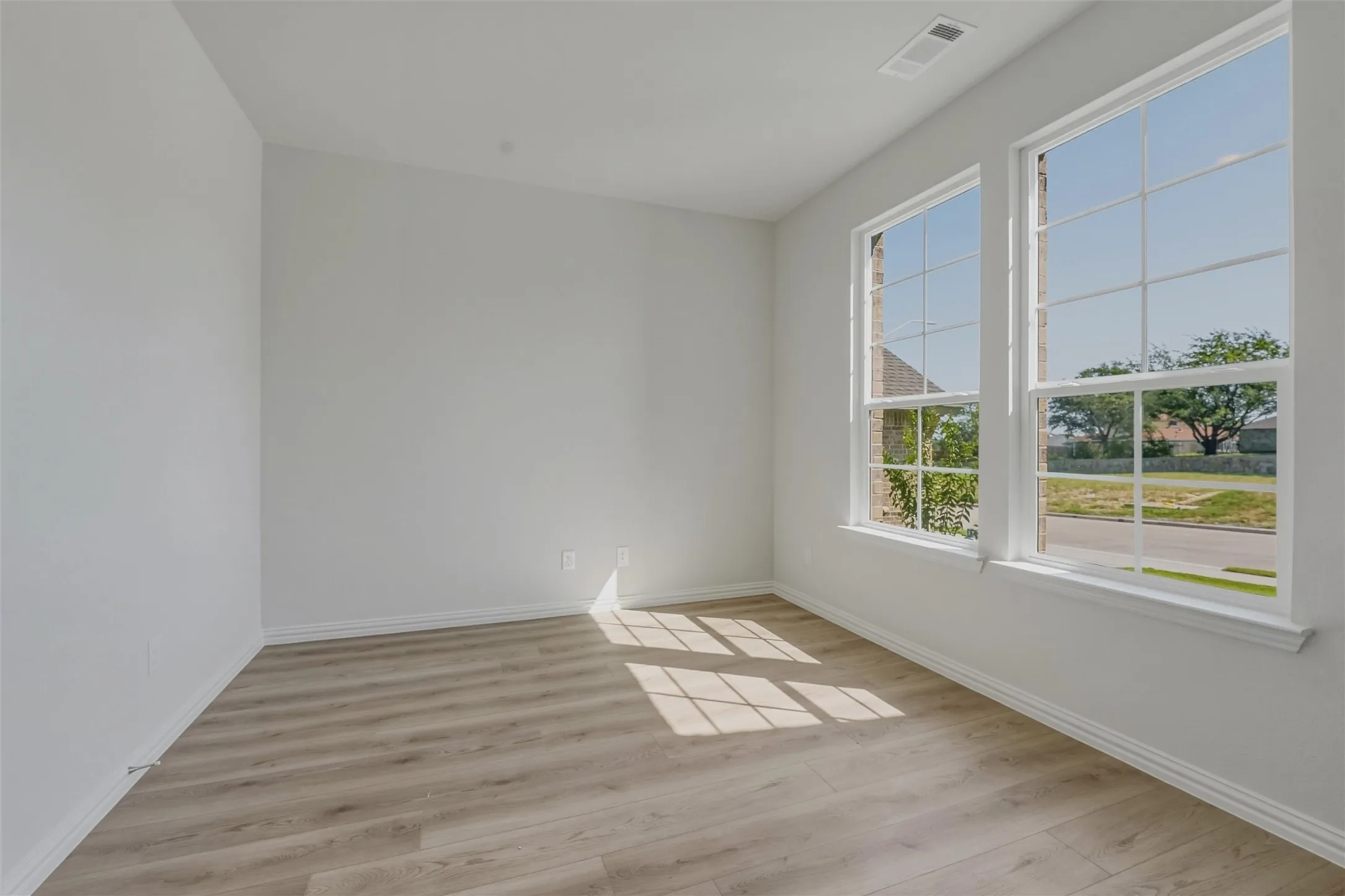 Spacious room featuring two large windows, wood-finish flooring, white baseboards, and neutral wall paint