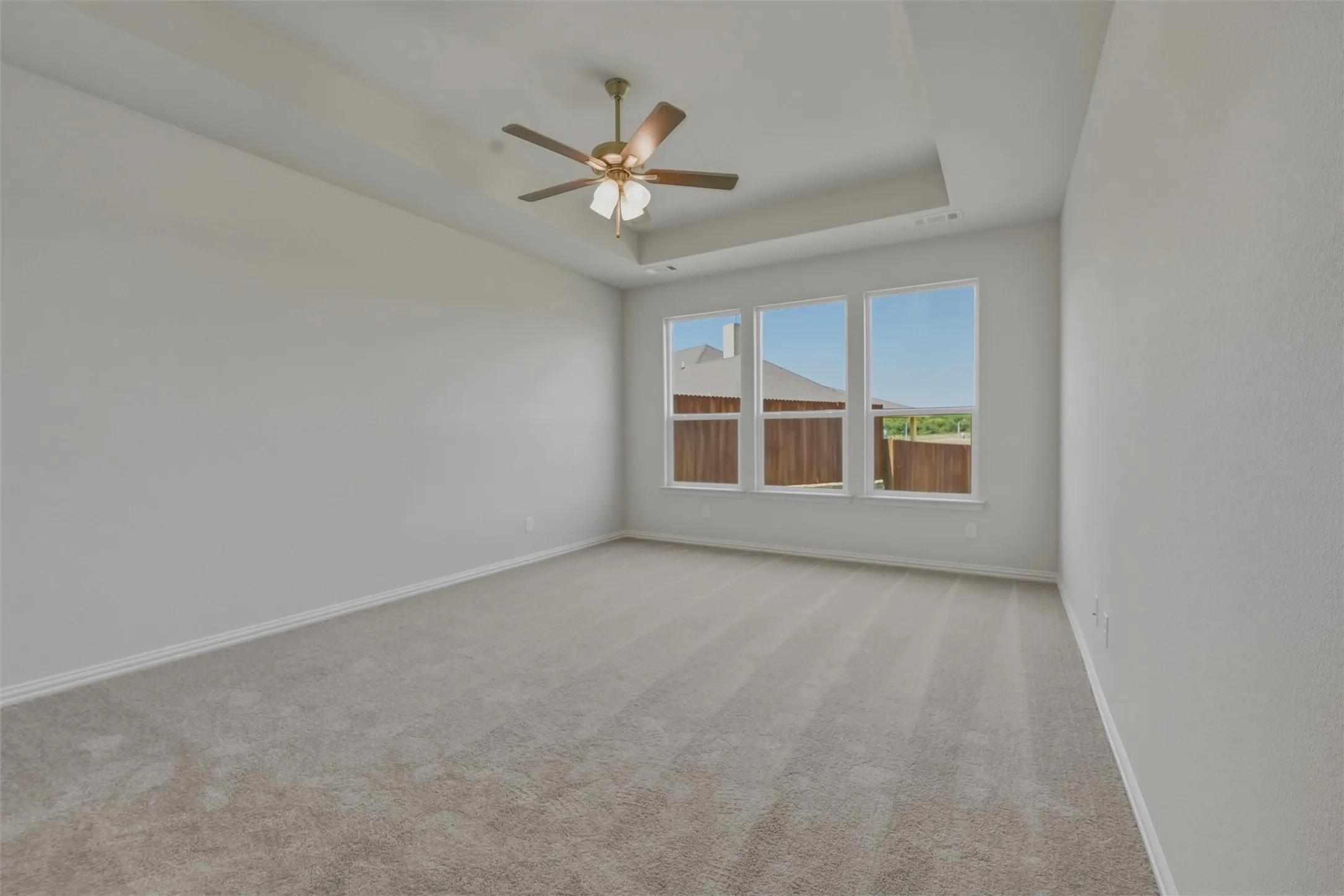 Spacious interior room featuring light-toned carpeting, a tray ceiling, and a ceiling fan with integrated lighting