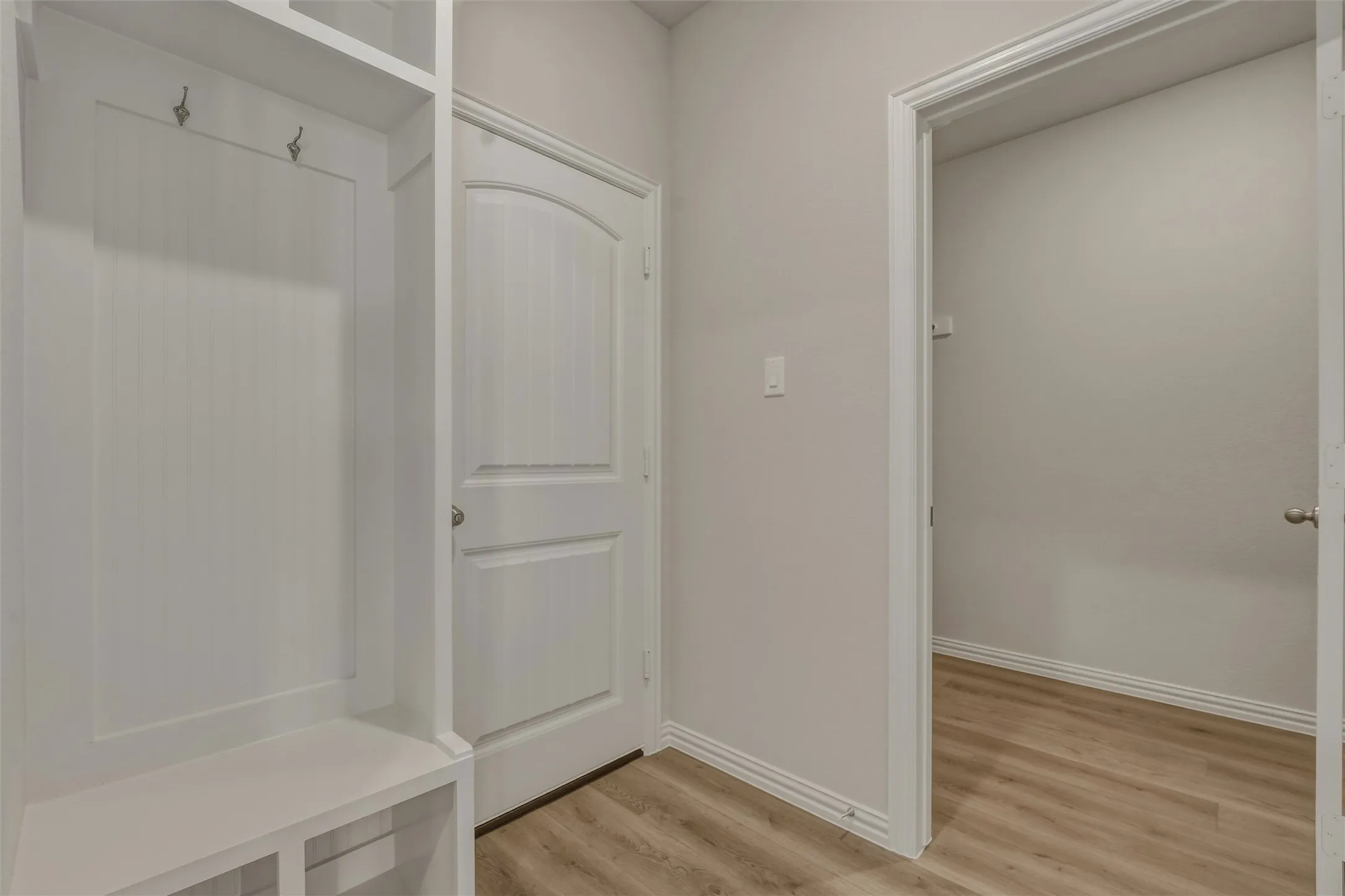 Built-in mudroom bench with coat hooks and overhead storage, alongside a paneled interior door, wood-finish flooring, and a recessed entryway