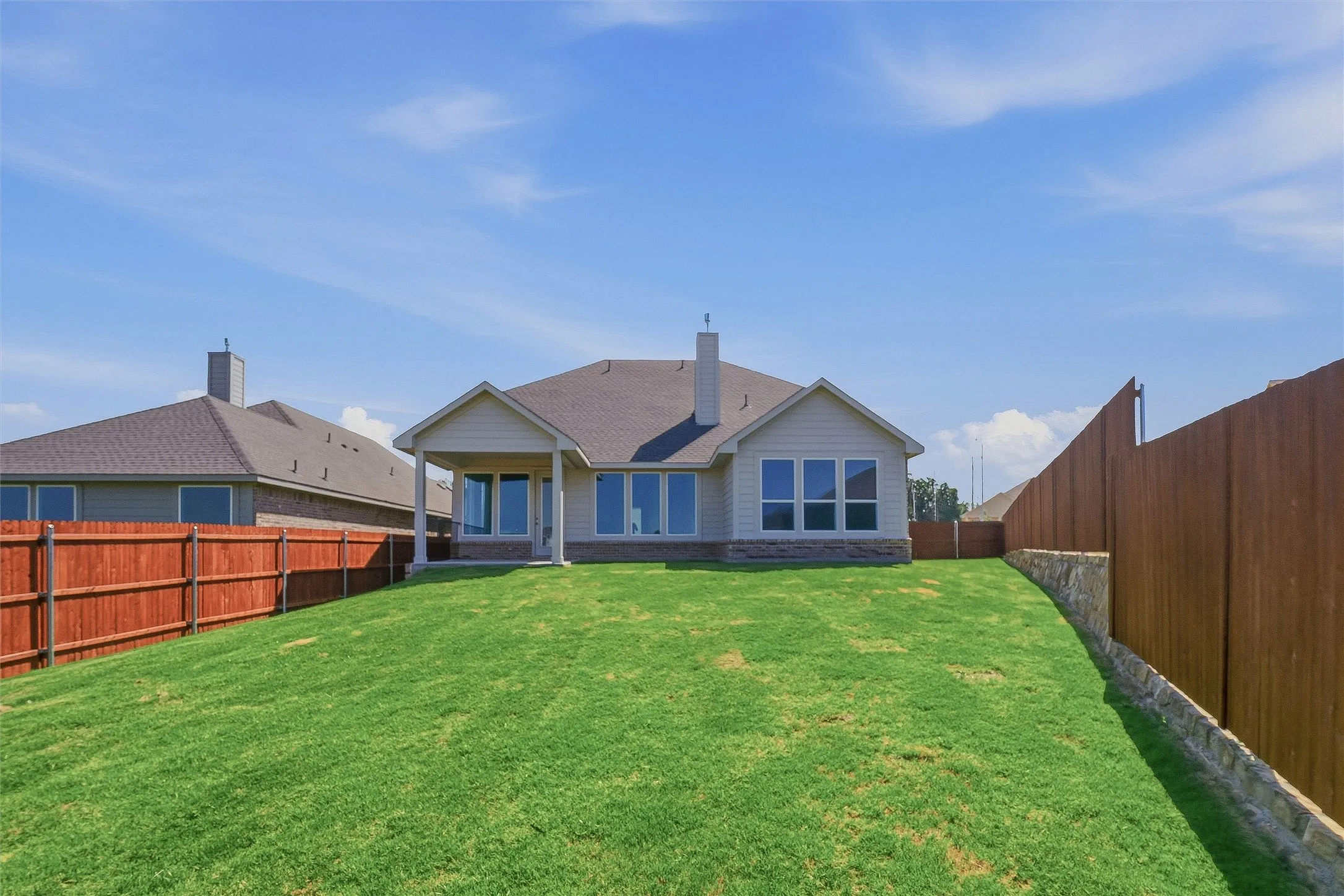 Expansive green lawn with a privacy fence and stone retaining wall