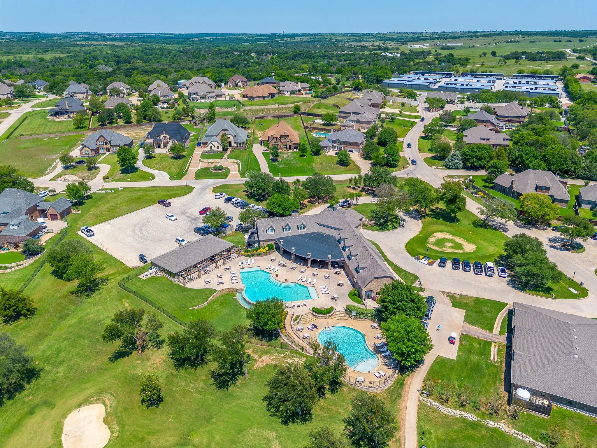 Aerial perspective showcasing a residential community with abundant green spaces, club house, and pools.