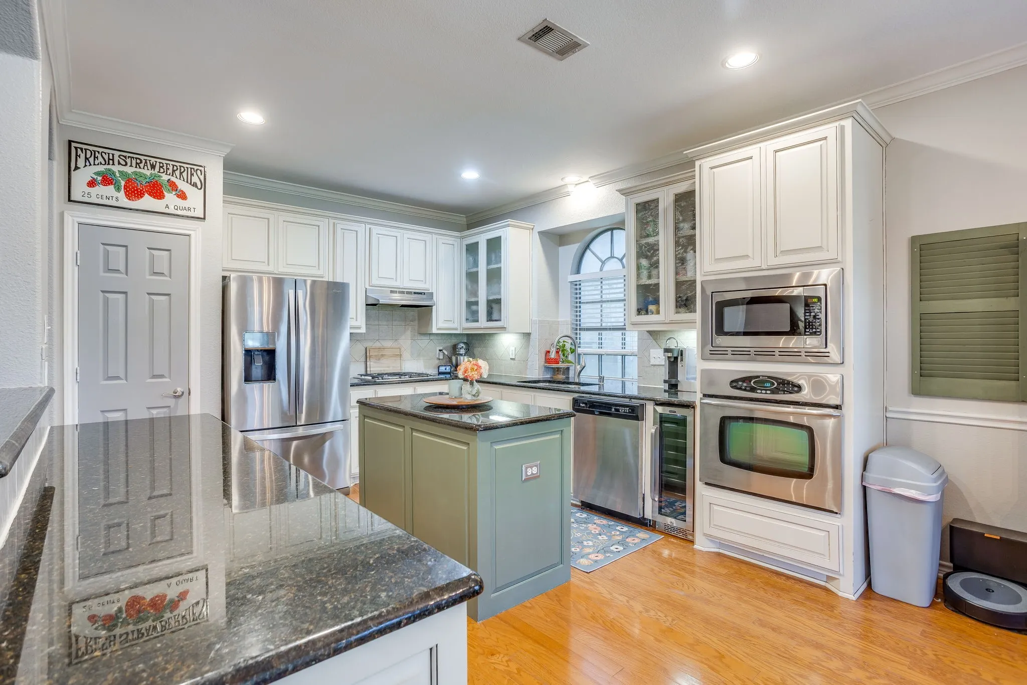 Kitchen featuring wood-finish flooring, dark granite countertops, stainless steel appliances, and white cabinetry