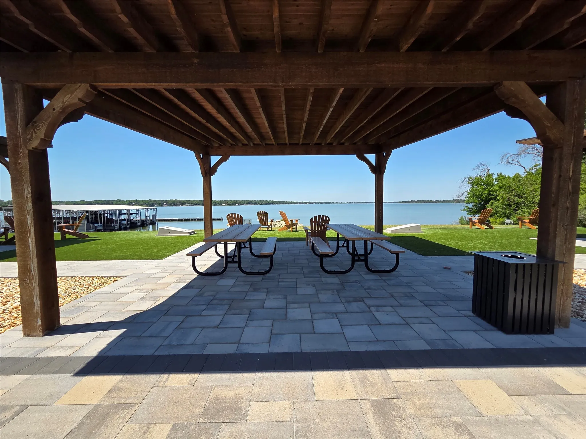 Expansive lakefront setting featuring a timber-framed pergola, paver patio, manicured lawn, and a boat dock with slips