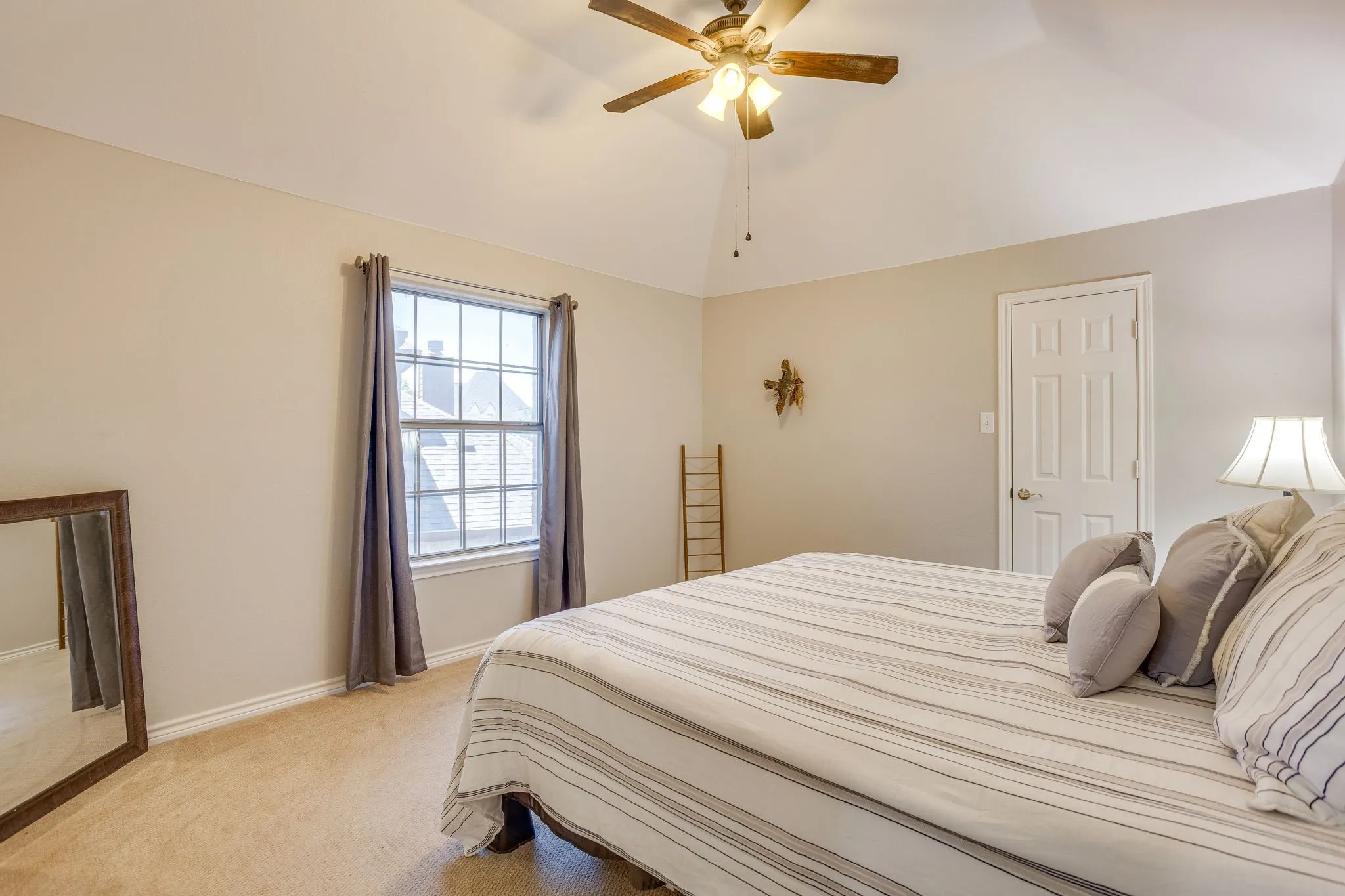 Vaulted ceiling with a wood-finish ceiling fan, neutral wall paint, white trim, and carpeted flooring