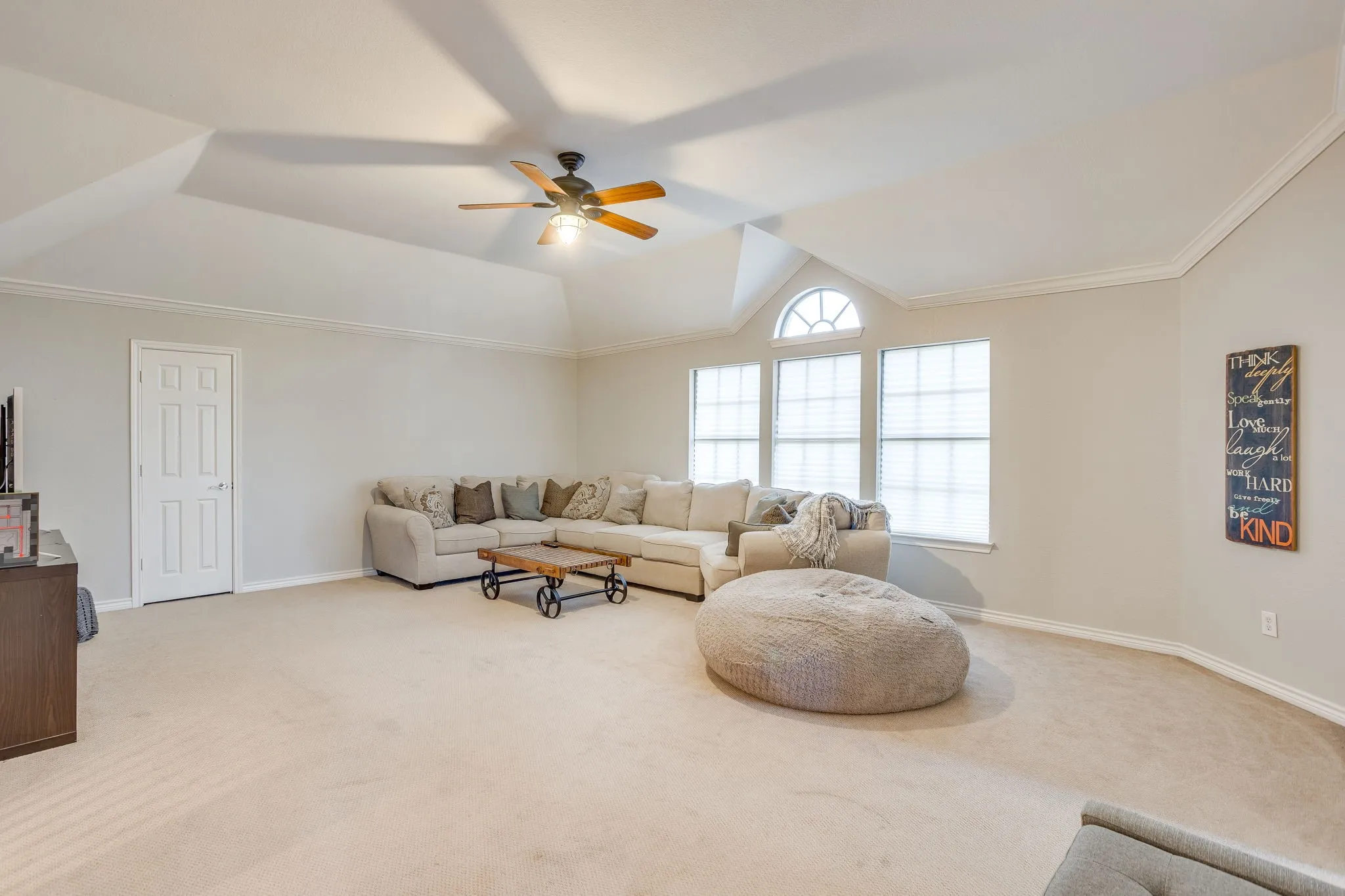 Spacious room featuring vaulted ceilings, crown molding, a ceiling fan, and multiple windows including an arched transom