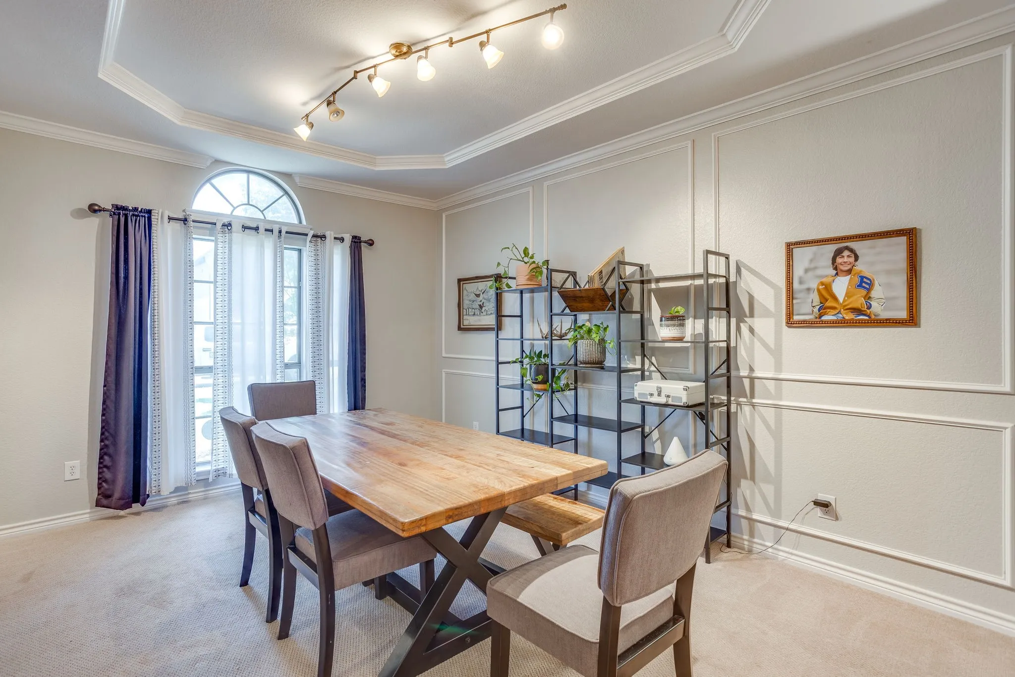 Tray ceiling with crown molding, track lighting, and a large arched window