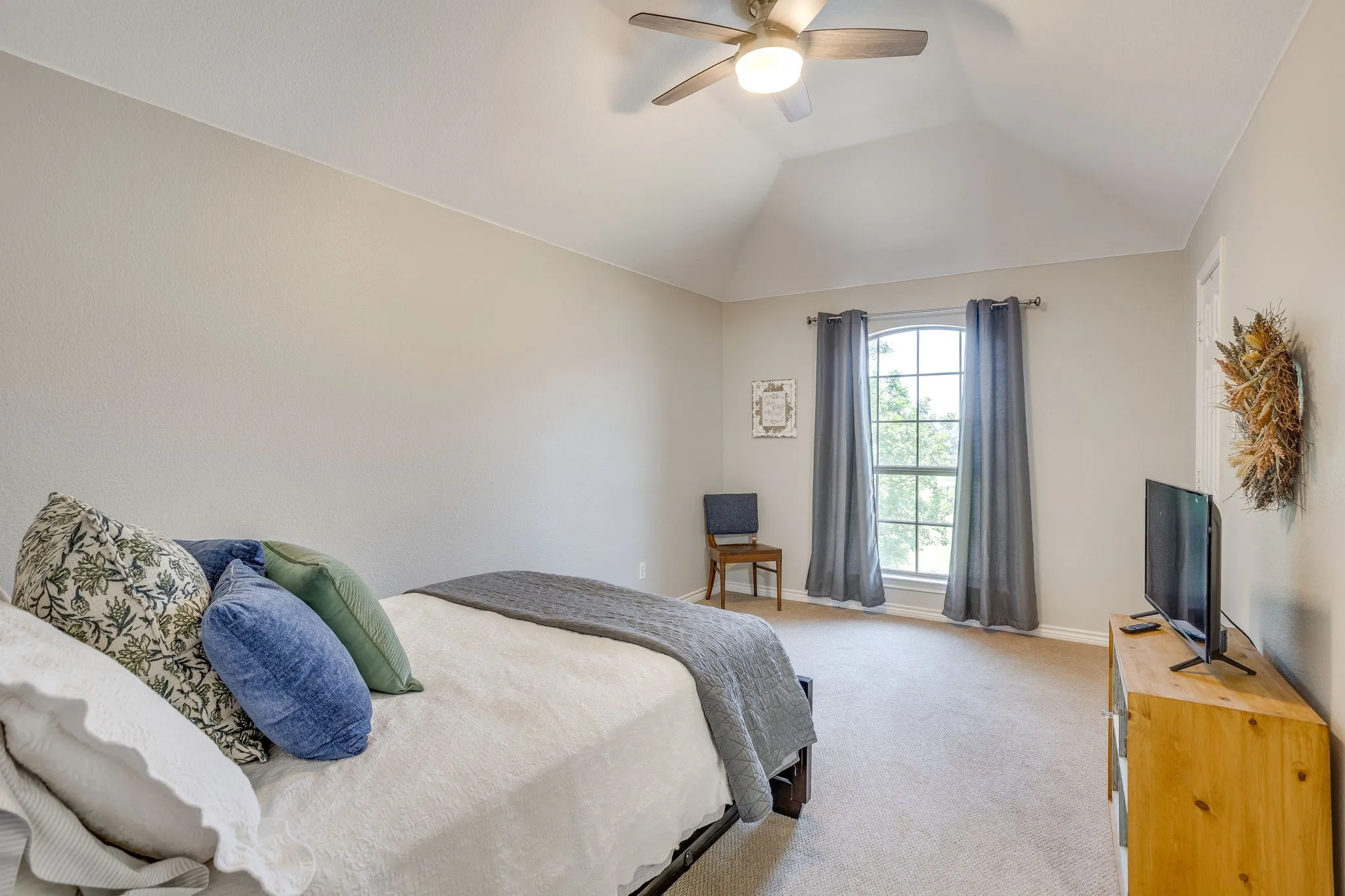 Arched window with gray drapes, vaulted ceiling, and ceiling fan with integrated lighting