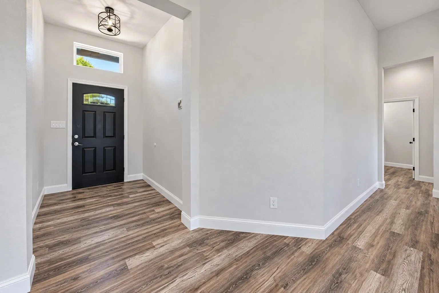 Entryway featuring a black paneled door with glass inserts, a transom window, wood-finish flooring, white walls, and a black metal semi-flush mount light fixture