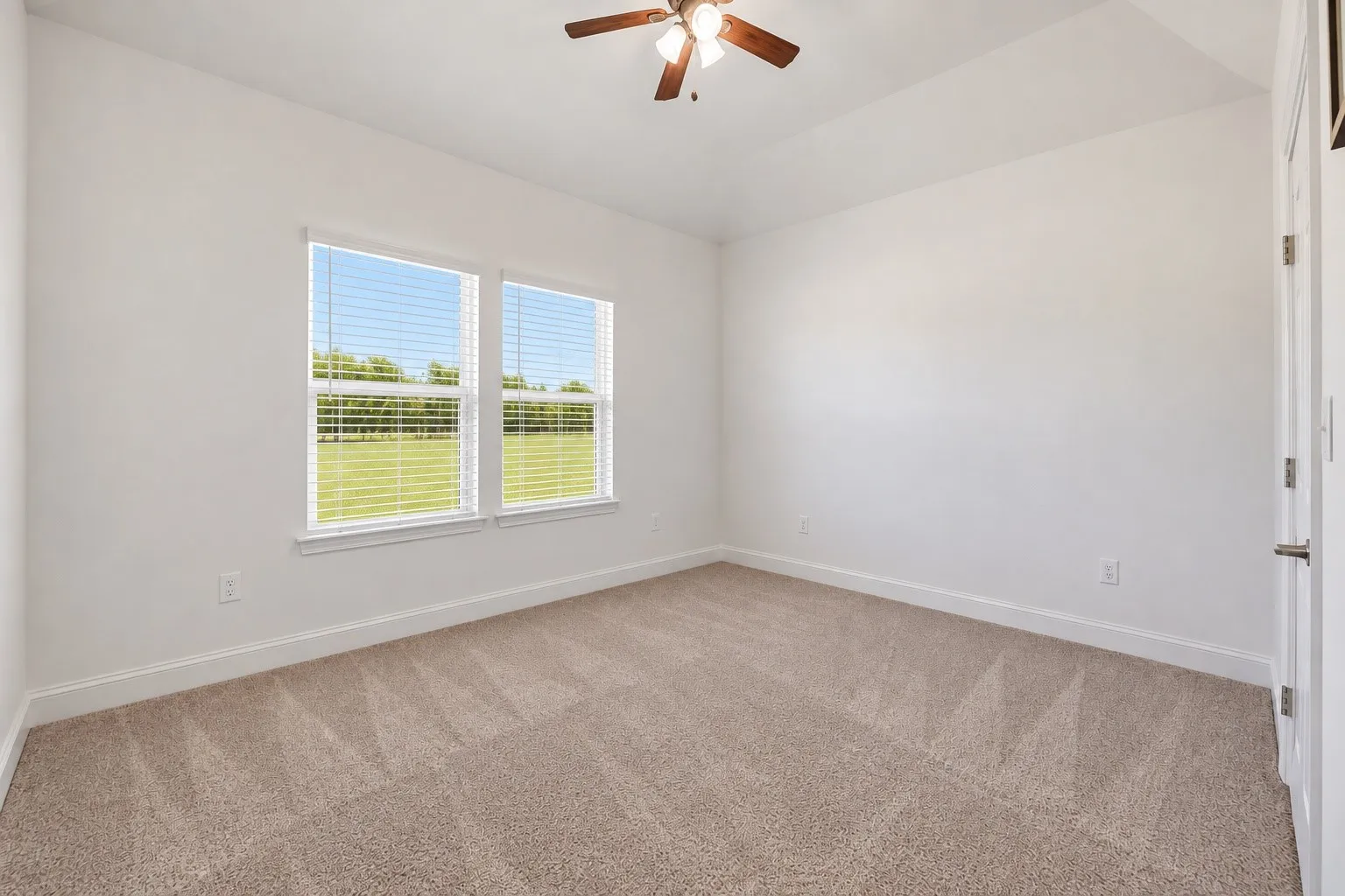 Room featuring neutral tone carpeting, white walls, two windows with blinds, a ceiling fan with integrated lighting, and a white interior door