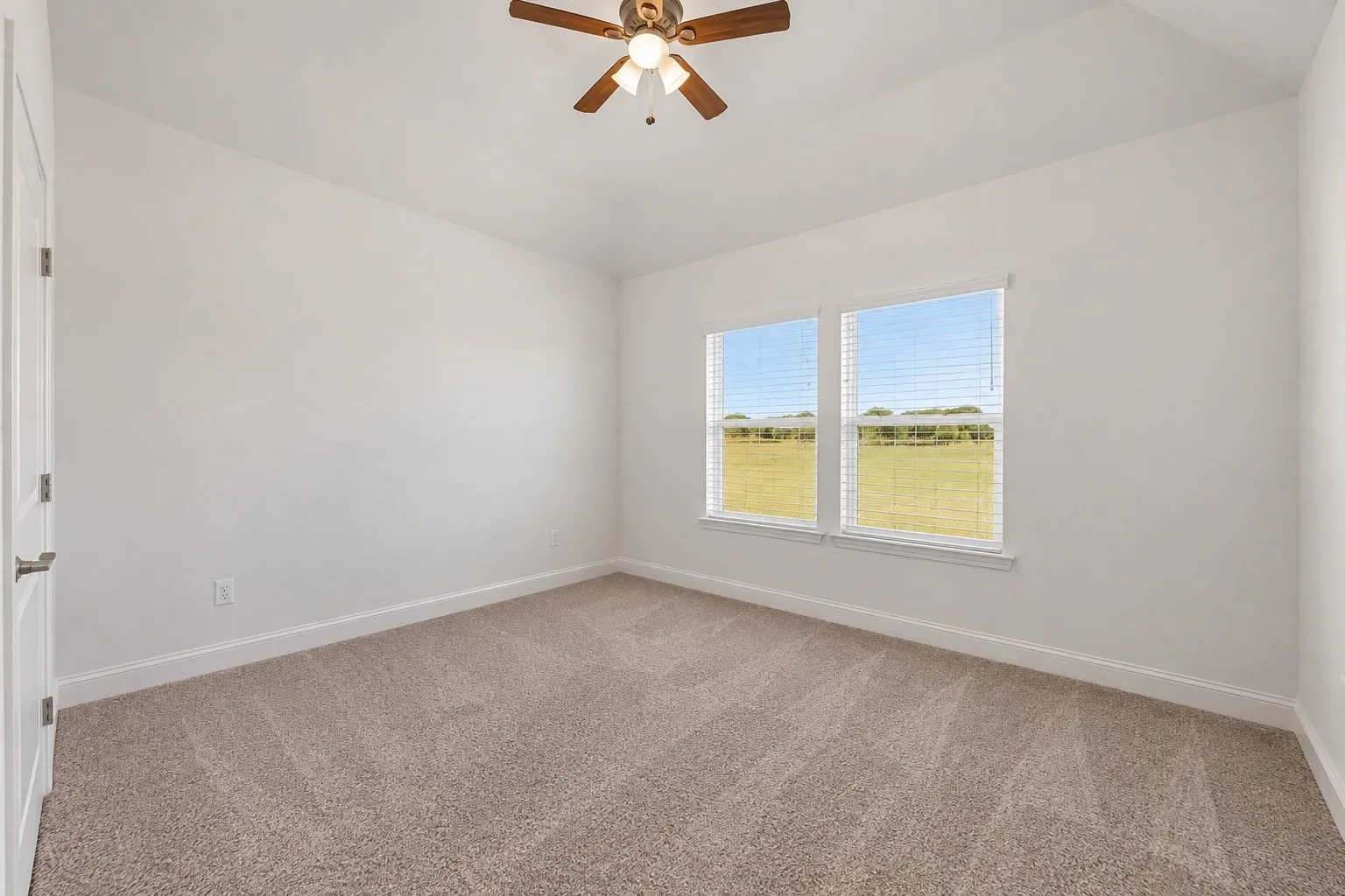 Neutral-toned carpet flooring, two windows with blinds, white walls, and a ceiling fan