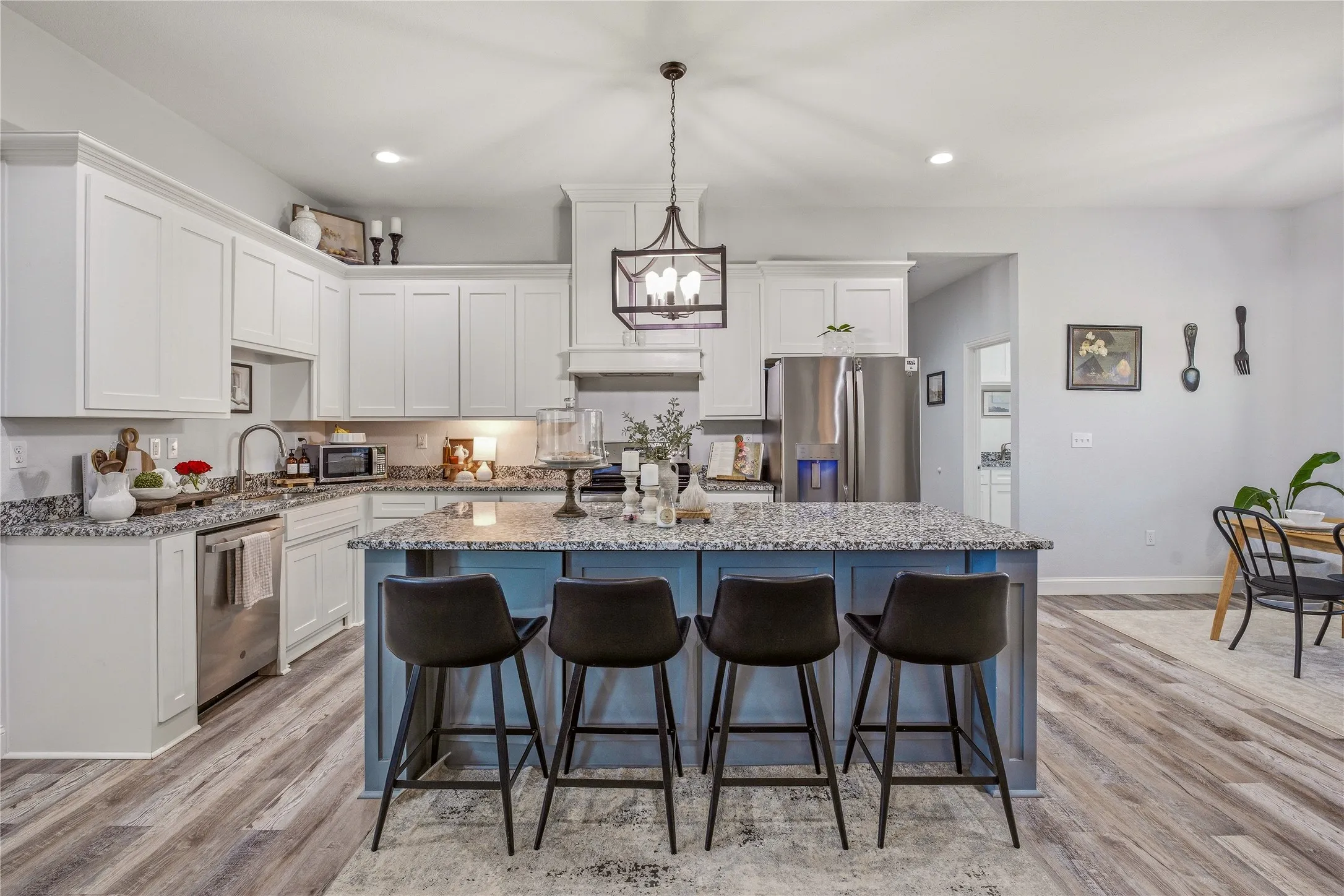 Kitchen featuring white cabinetry, wood-finish flooring, a central island with countertop seating, stainless steel appliances, and a pendant light fixture