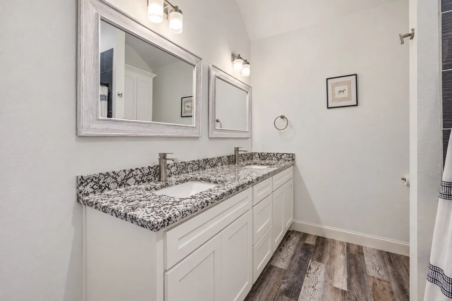 Double vanity with white shaker-style cabinetry, undermount sinks, speckled stone countertops, and wood-finish flooring