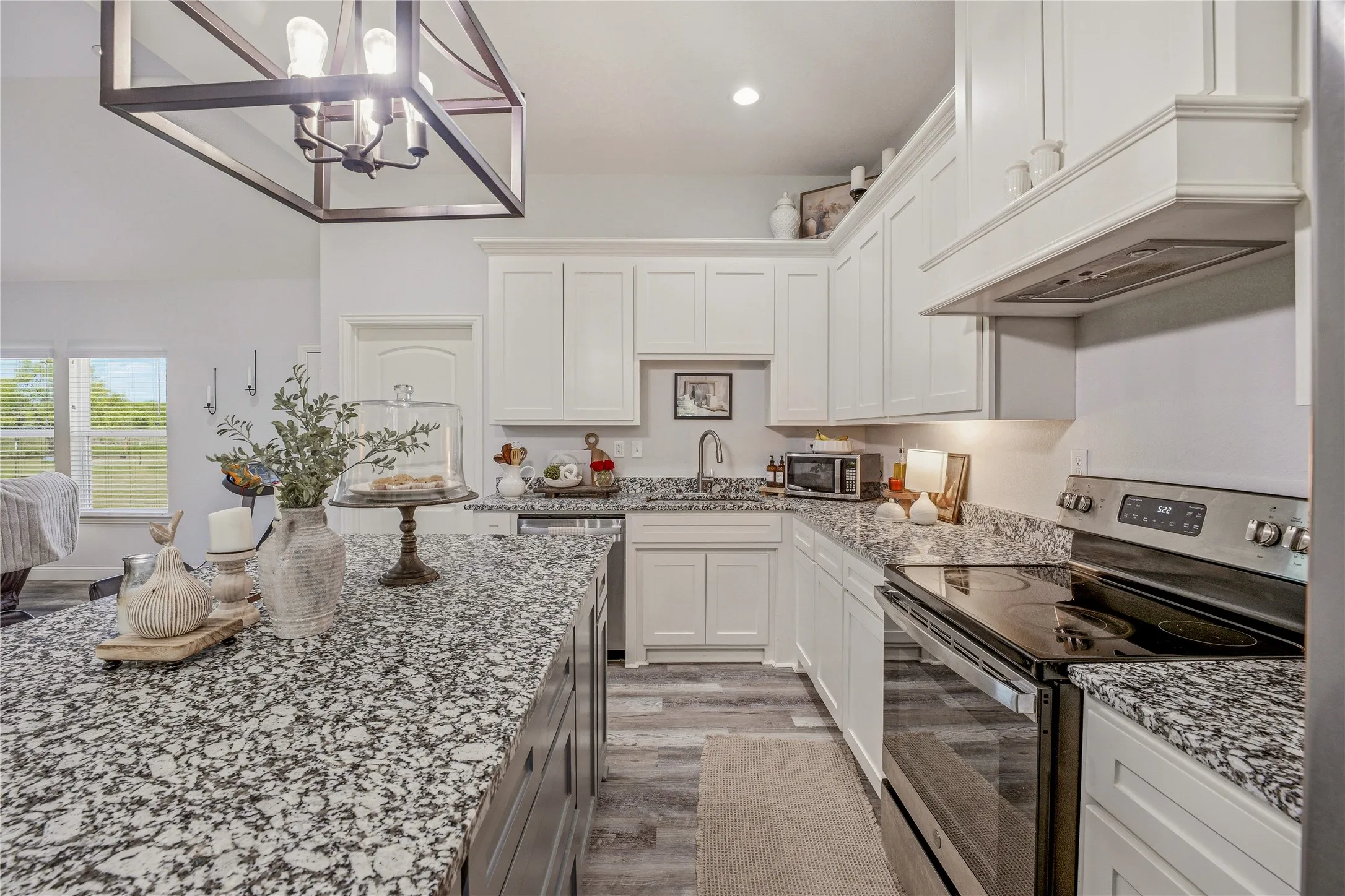 Spacious kitchen featuring an island with a speckled countertop, white cabinetry, stainless steel appliances, and wood-finish flooring