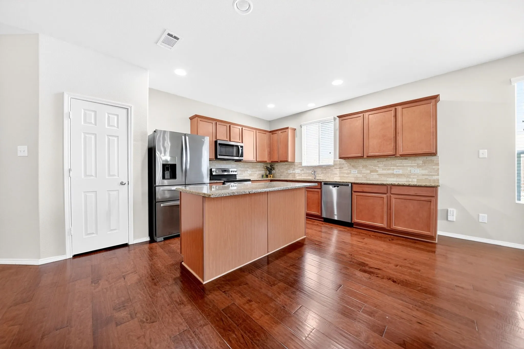 The kitchen features stainless steel appliances, a spacious kitchen island, granite countertops, and a decorative backsplash.