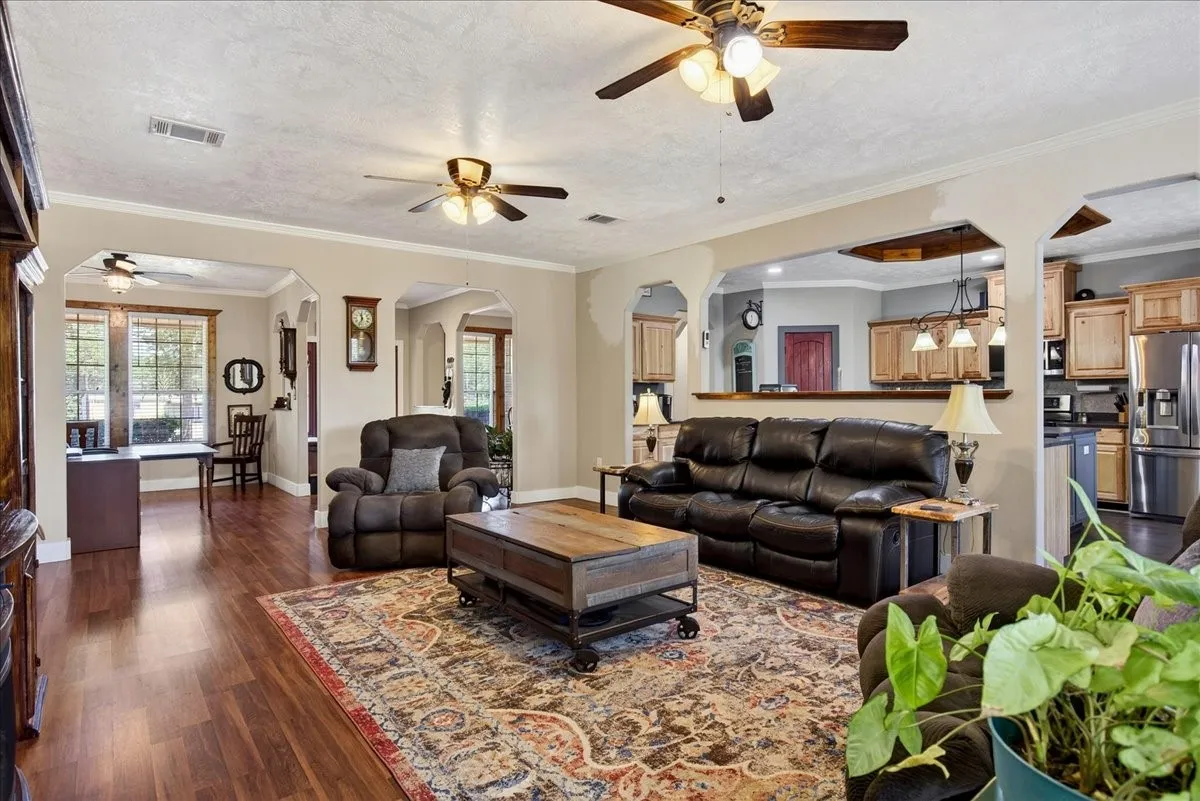 Spacious living area featuring wood-finish flooring, light-toned walls, and multiple ceiling fans. Open concept floor plan.