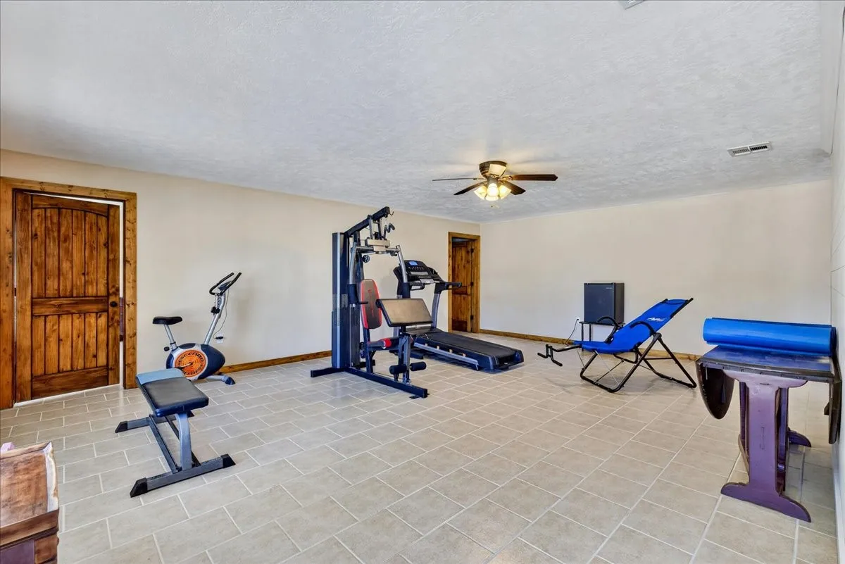 Basement room featuring neutral-toned walls, tile flooring, and rustic wood-paneled doors. Right now this multi purpose space is the exercise room - BUT what would you do with this dream space?