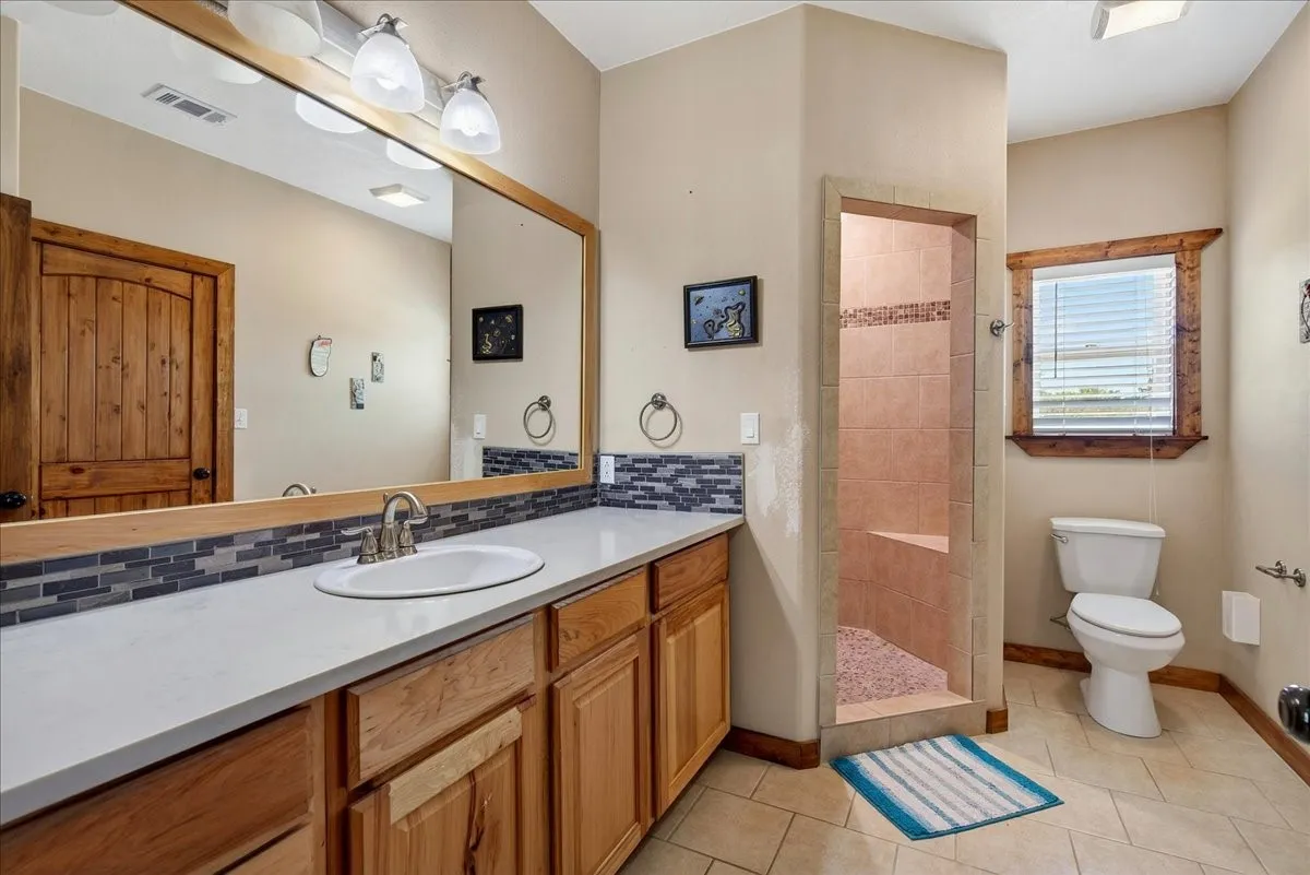 2nd Primary Bathroom on level 1 featuring an oak vanity with light quartz countertop and undermount sink, backsplash, big mirror, cabinets and drawers. Large oversize walk-in shower with pebble stone, oversize walk-in closet, tile floor