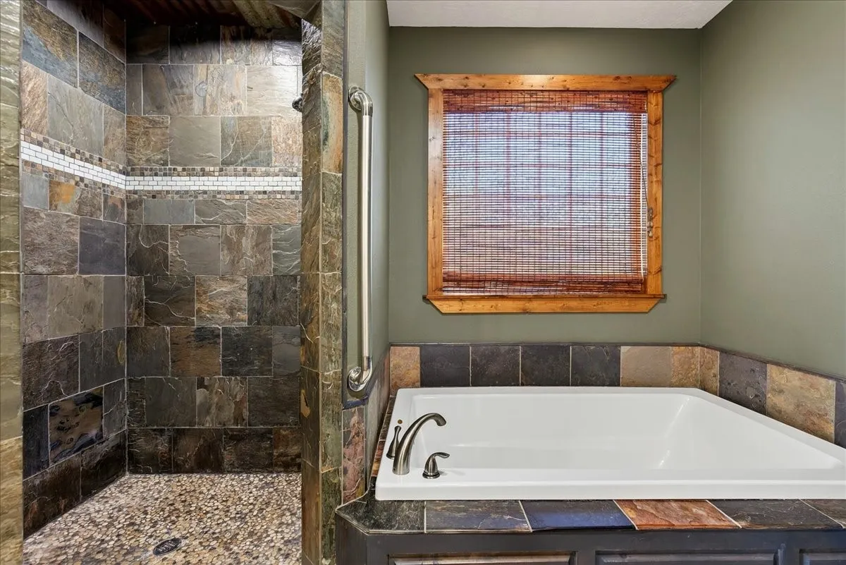 Walk-in shower with natural stone tile and pebble flooring, oversize soaker tub.