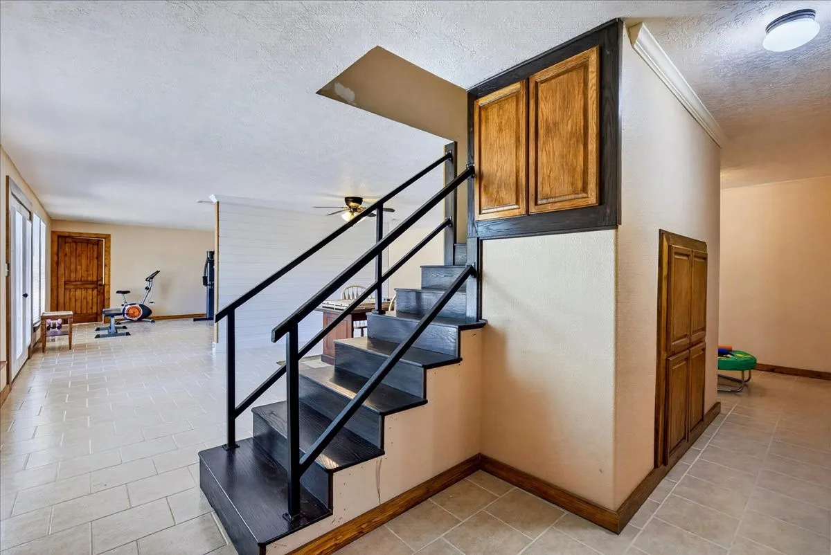 WOW - fully air conditioned basement adds another 1565SF. Open-concept interior featuring a prominent staircase with black metal railings, wood finish treads, and integrated under-stair cabinetry. Large open spaces on each side of staircase, a full bathoom, utility room, and 2 more bedrooms. French doors lead outside.