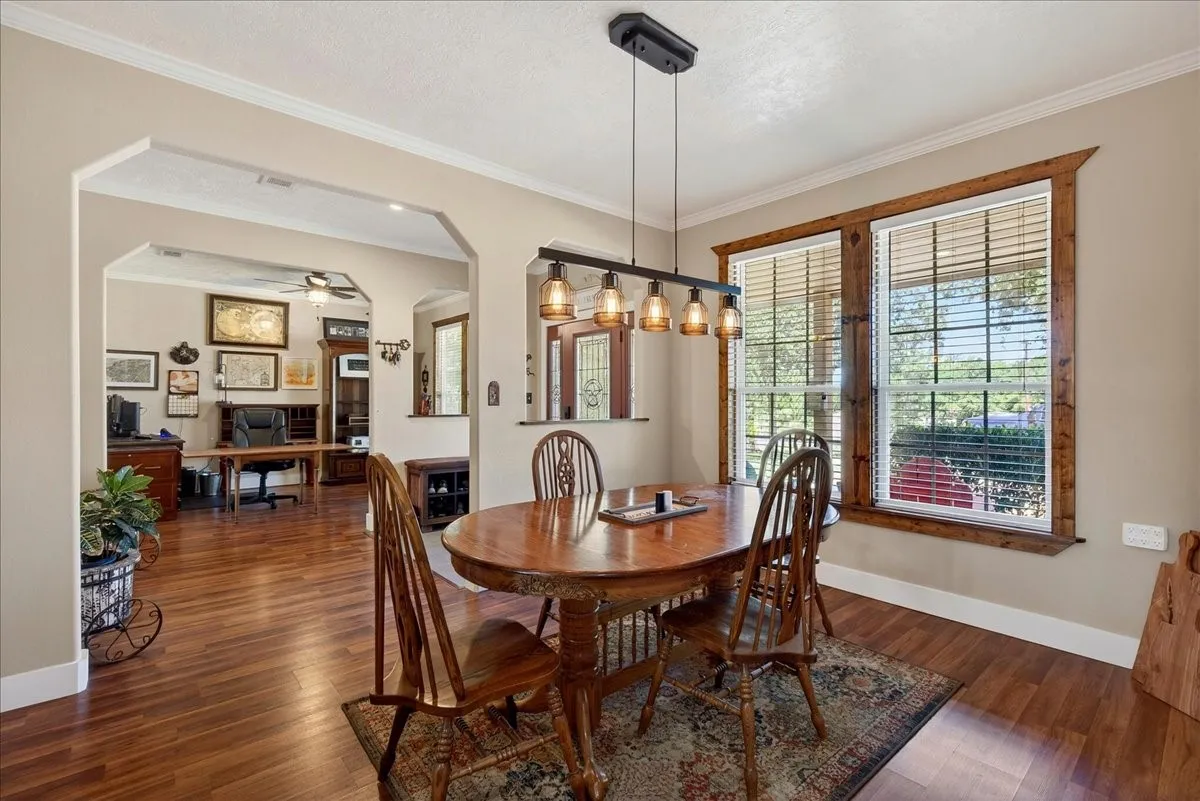 Dining area featuring wood-finish flooring, a linear pendant light fixture with amber glass shades, and two windows framed with natural wood trim, open to living-office-kitchen.