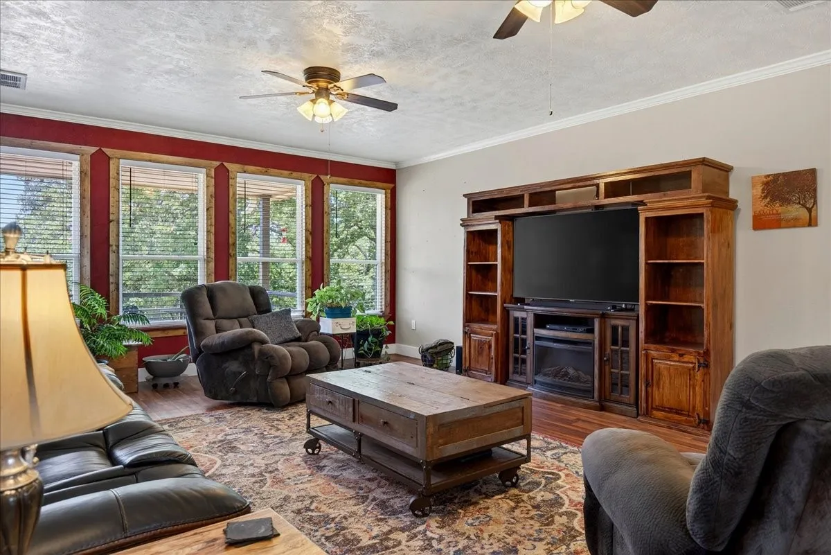 Living area featuring a multi-panel window wall with wood trim and red accent wall, ceiling fans, wood laminate floors throughout. Open concept floor plan.