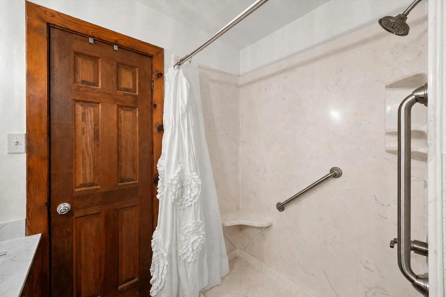 Oversized tiled walk-in shower with grab bar and built-in shelving.
