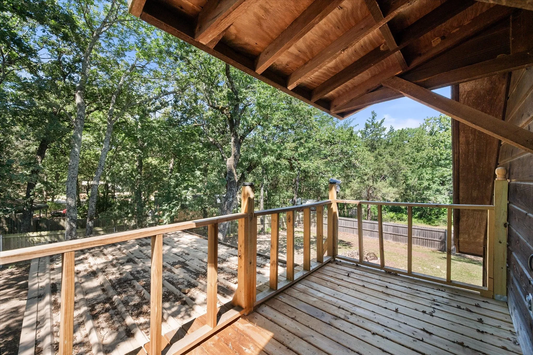 Covered upper balcony surrounded by mature trees for peaceful outdoor relaxation.