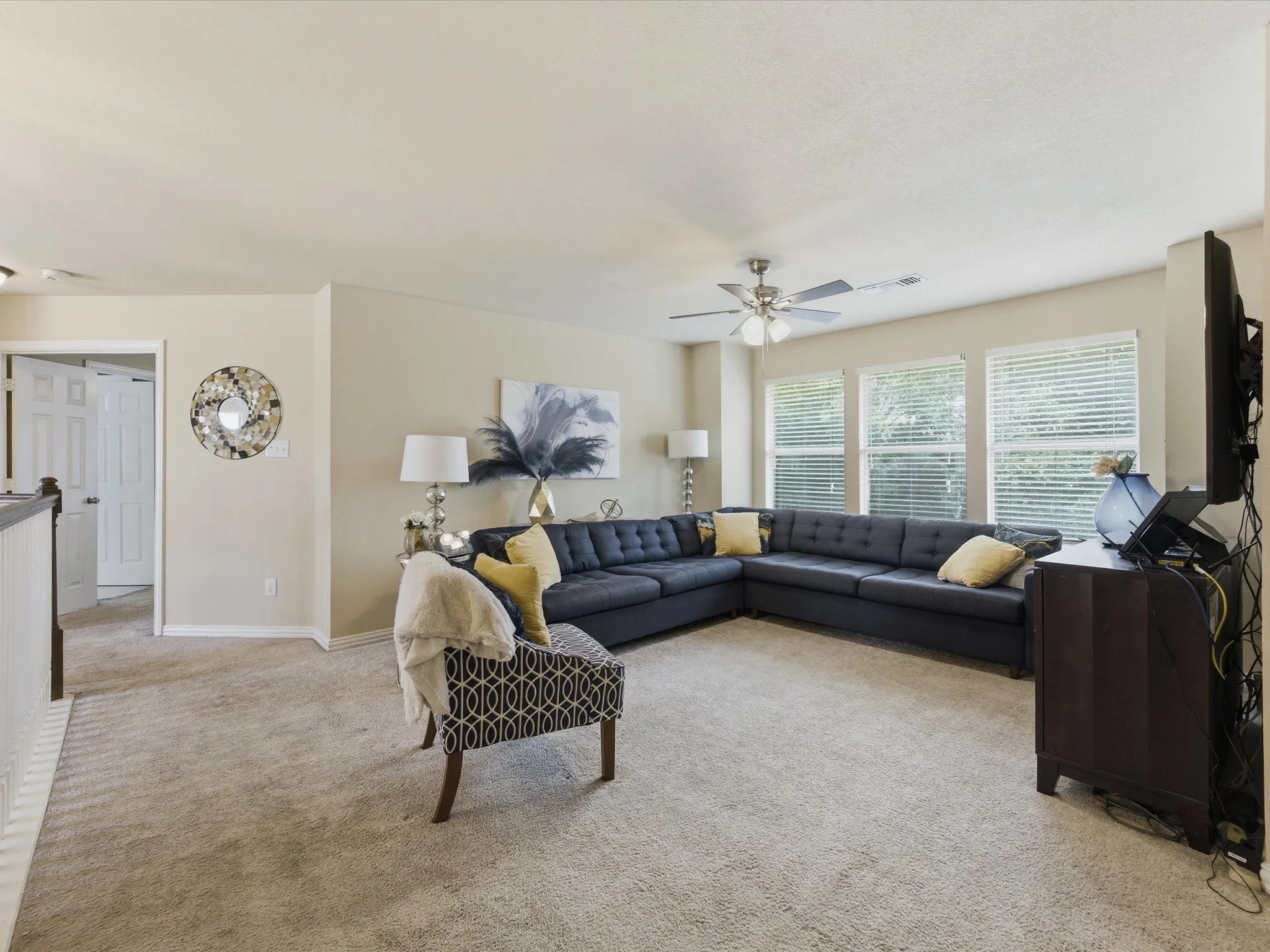 Carpeted secondary living space with multiple windows featuring blinds, a ceiling fan, and painted walls