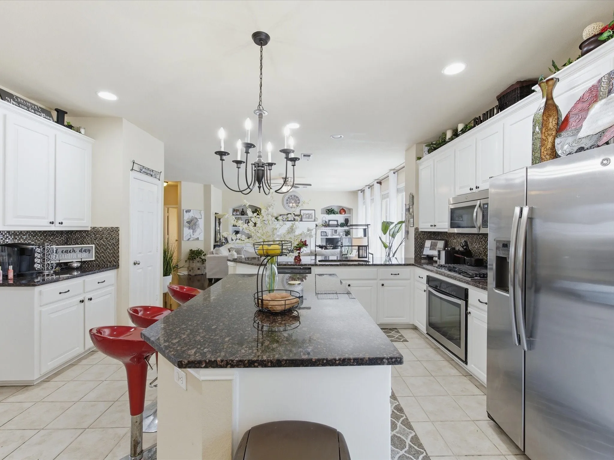 Kitchen featuring a dark granite island and perimeter countertops, white cabinetry, stainless steel appliances, a mosaic tile backsplash, and tile flooring