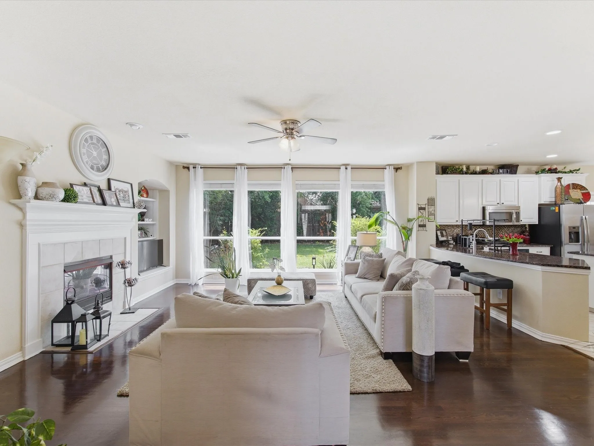 Bright open-concept living area with dark wood-finish flooring, a white mantel fireplace, and built-in shelving