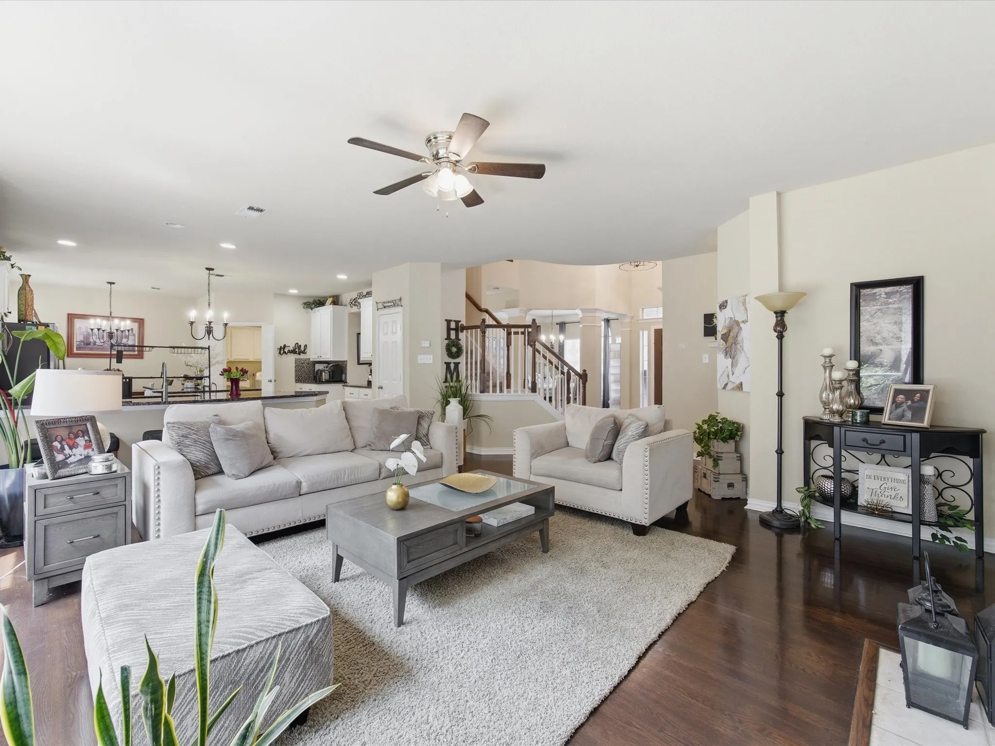Expansive living area with rich wood-finish flooring, a ceiling fan, and staircase with white risers and dark wood handrails
