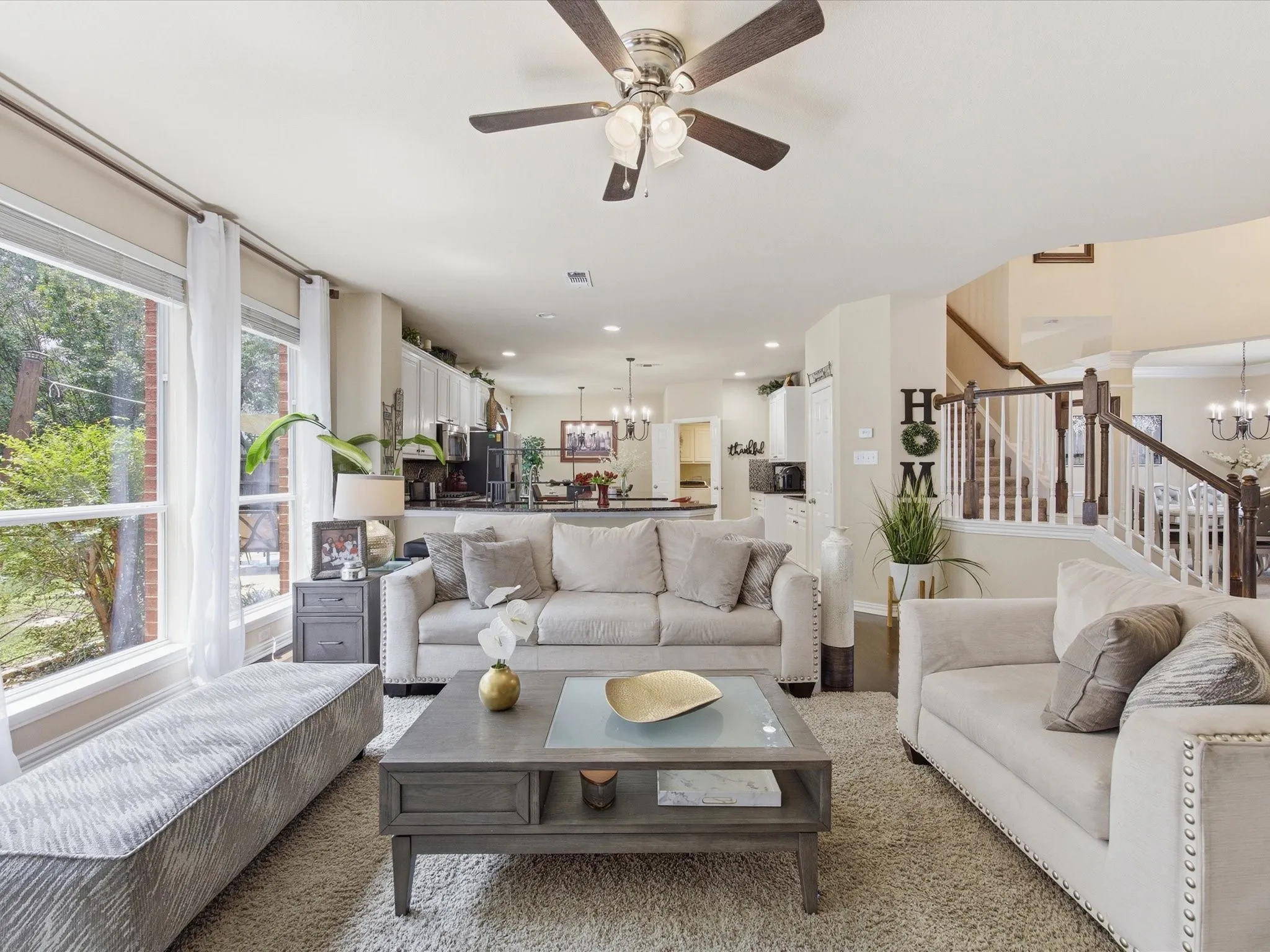Open-concept living space featuring a ceiling fan, large windows, recessed lighting, and a staircase with wood newel posts and railings