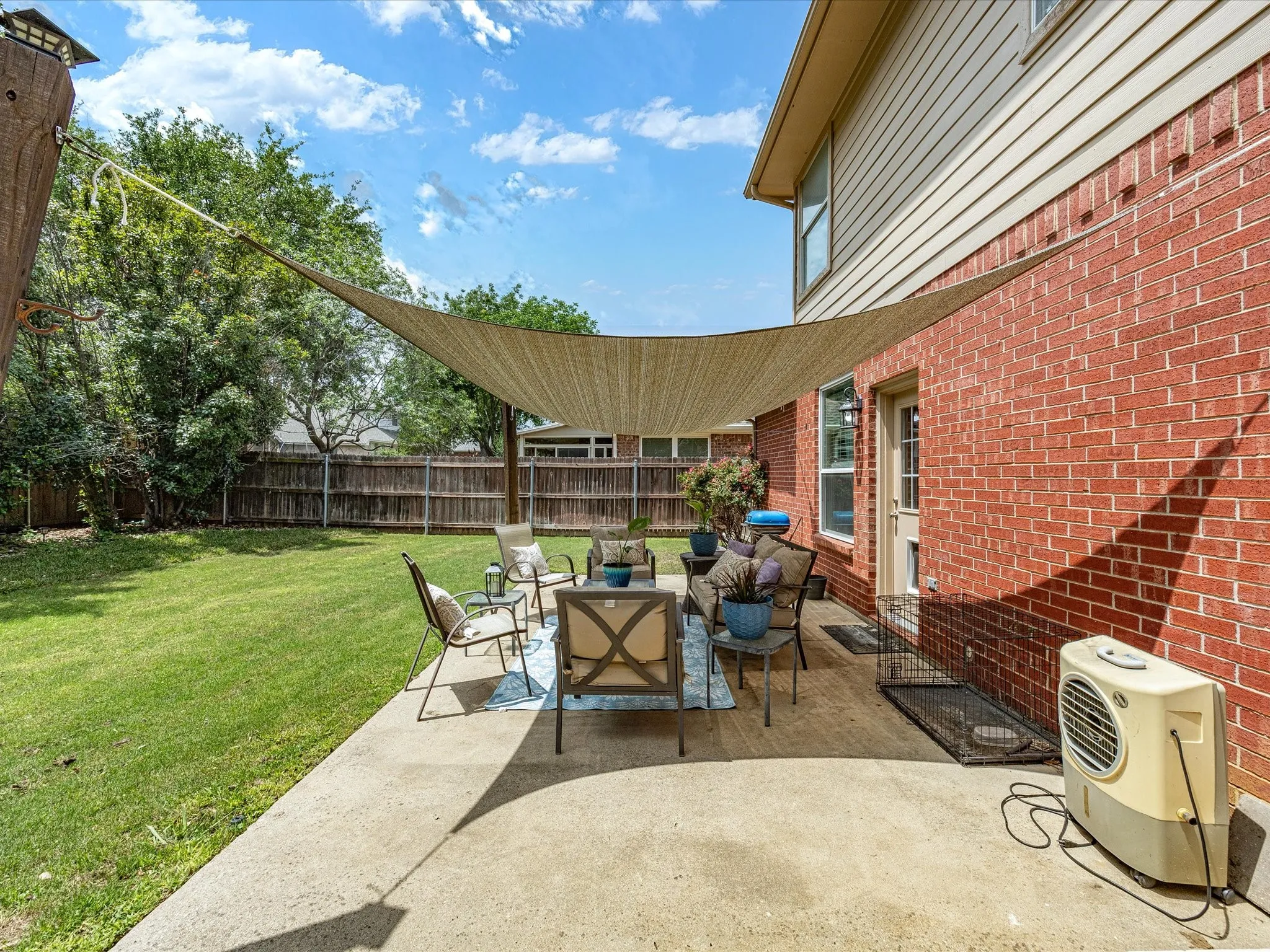 Spacious concrete patio featuring a shade sail, red brick exterior, siding upper level, and a wood privacy fence